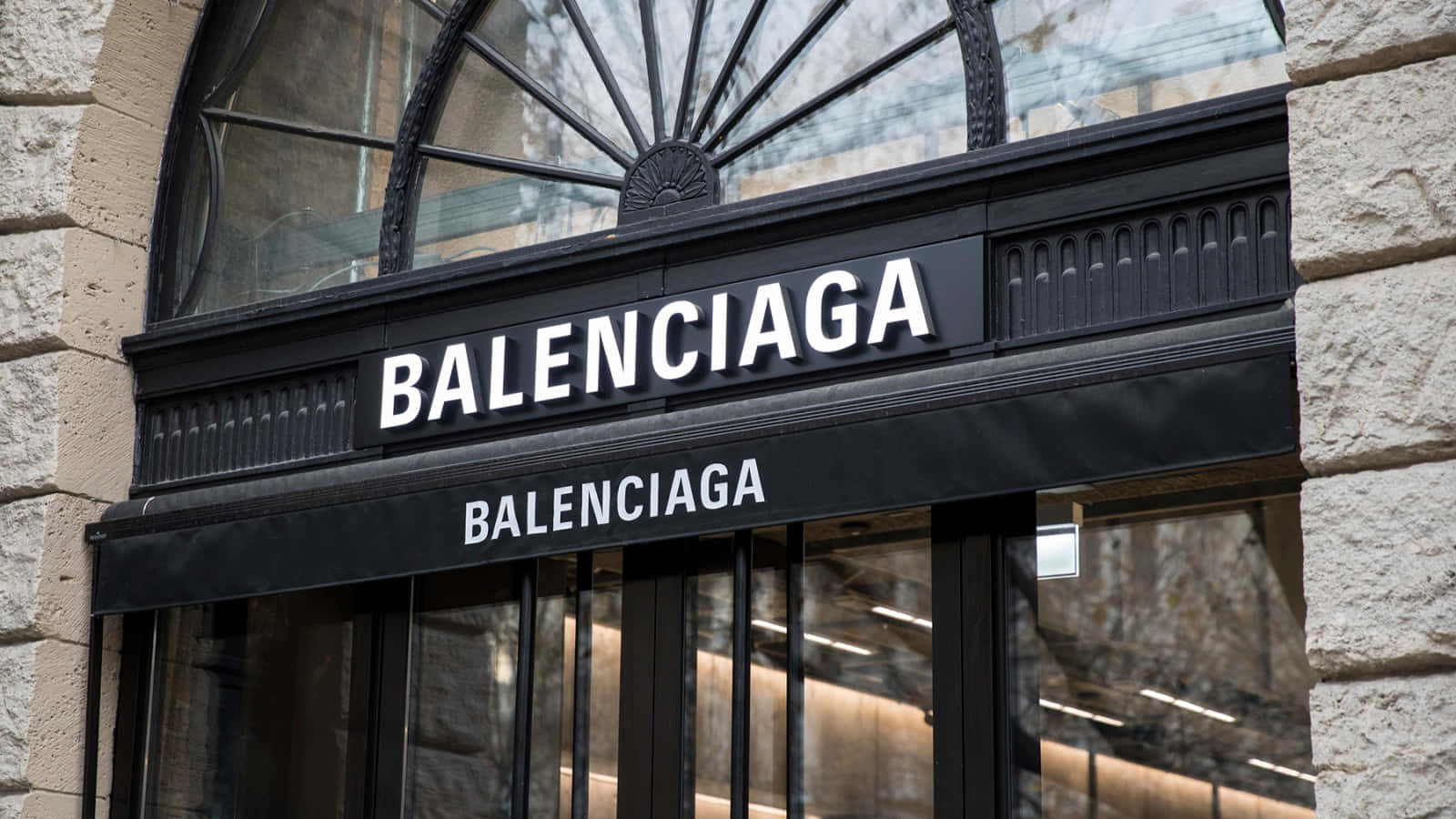 專業中帶點叛逆：Balenciaga 壁紙 — Balenciaga 店舖入口特寫，黑色招牌上帶有粗體白色字體，以石頭和拱形玻璃框住。