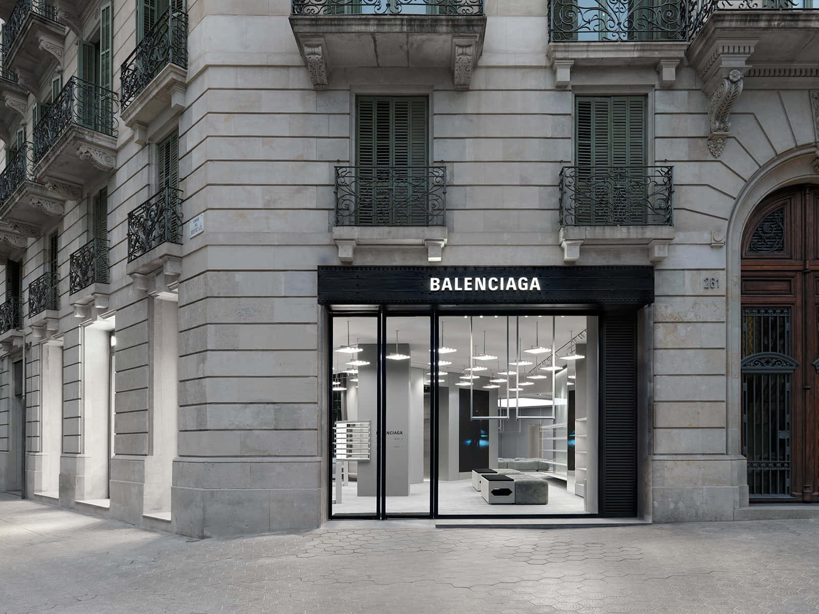優雅奢華的 Balenciaga 設計 壁紙 — 一間時尚的Balenciaga商店，設有黑色框玻璃門和極簡主義的室內照明，背景是帶有華麗陽台的歷史石建築。