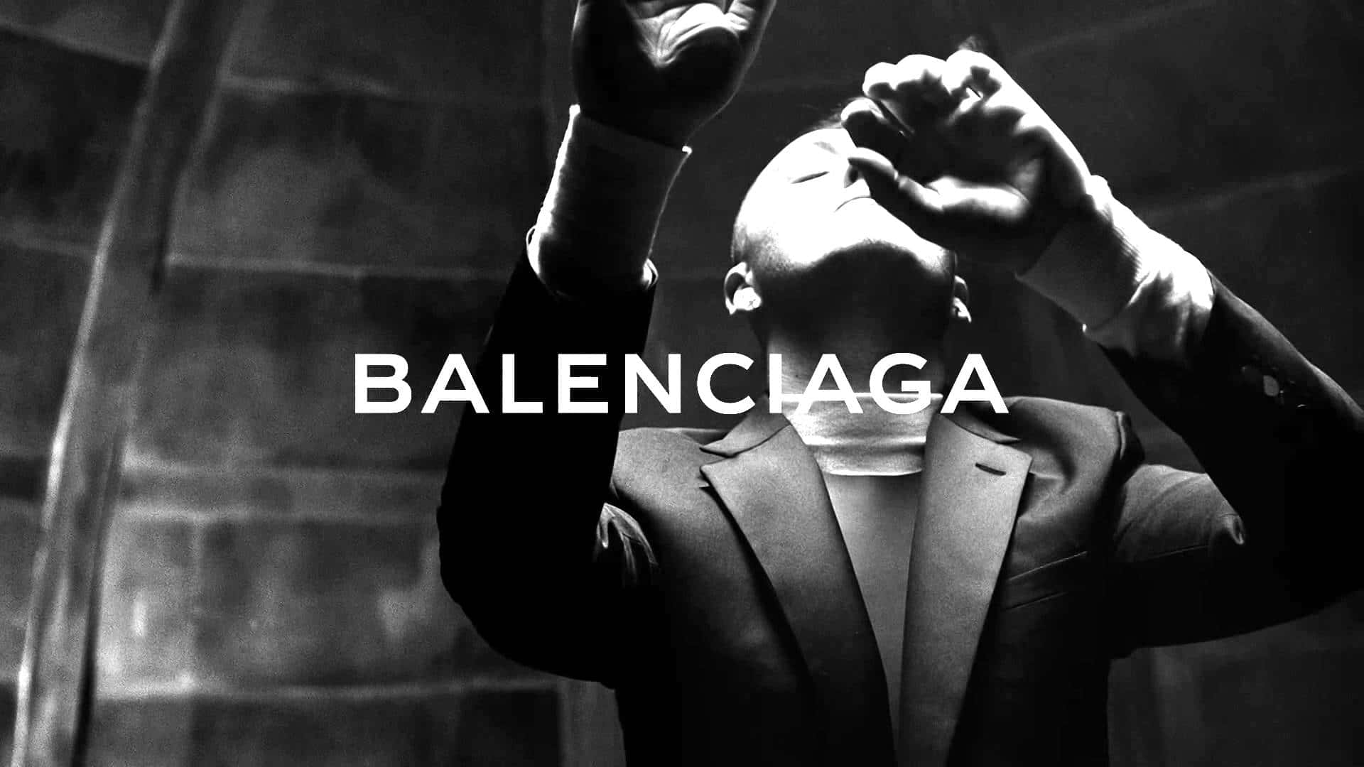 以 Balenciaga 穿出前衛時尚 壁紙 — 一名穿著西裝的男子在帶有 'BALENCIAGA' 文字的戲劇性黑白時尚廣告中舉起雙手。
