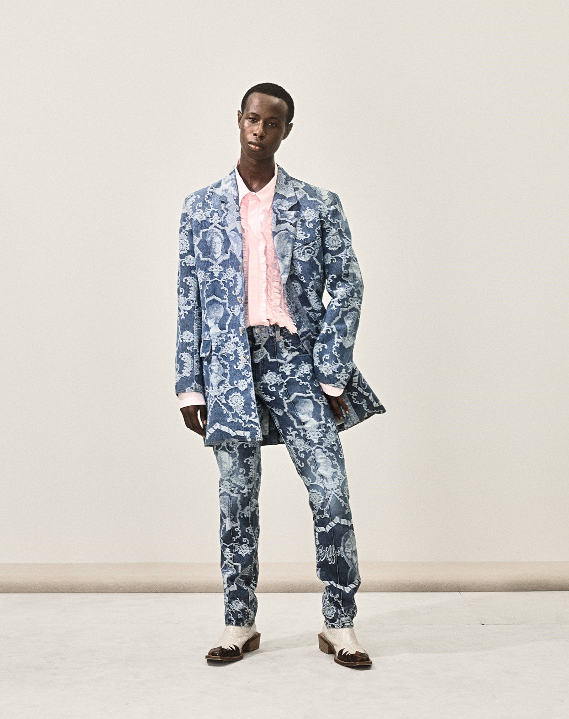 Balenciaga 蛇紋禮服西裝 壁紙 — 一名男子自信地站在純色攝影棚背景前，身穿藍色圖案西裝和粉紅色襯衫。