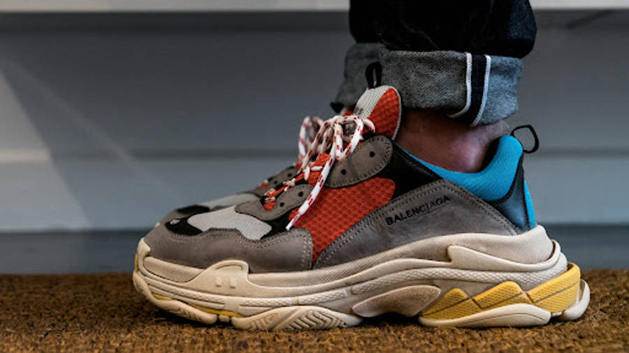 Balenciaga 跑步鞋 壁紙 — 一個人嘅腳部特寫，著住色彩繽紛嘅Balenciaga Triple S波鞋，企喺有紋理嘅棕色地板上面。