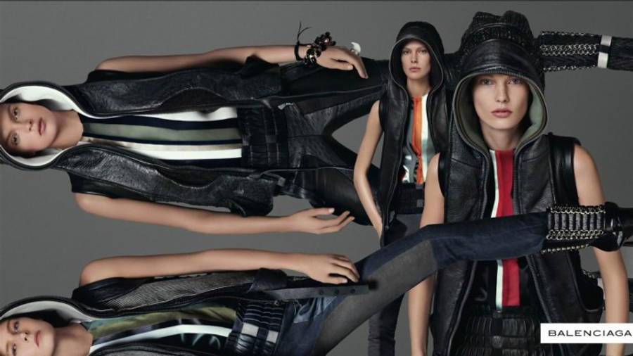 Balenciaga 雜誌封面 壁紙 — 三位模特兒穿著前衛的黑色皮連帽衫和背心，在灰色中性背景前動感擺姿勢。