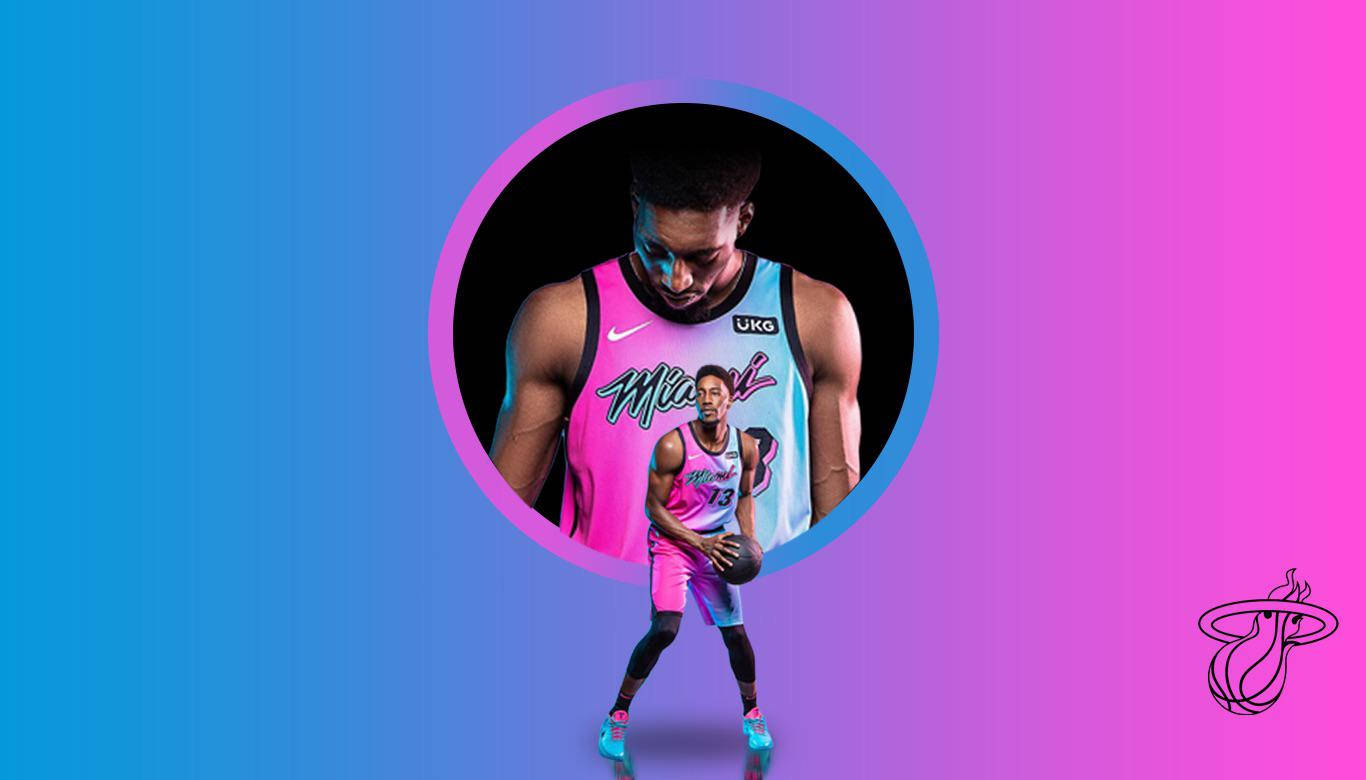 Bam Adebayo 藍粉漸層 壁紙 — 一名身穿邁阿密熱火球衣的籃球運動員自信地站在充滿活力的藍色和粉紅色漸變背景前。
