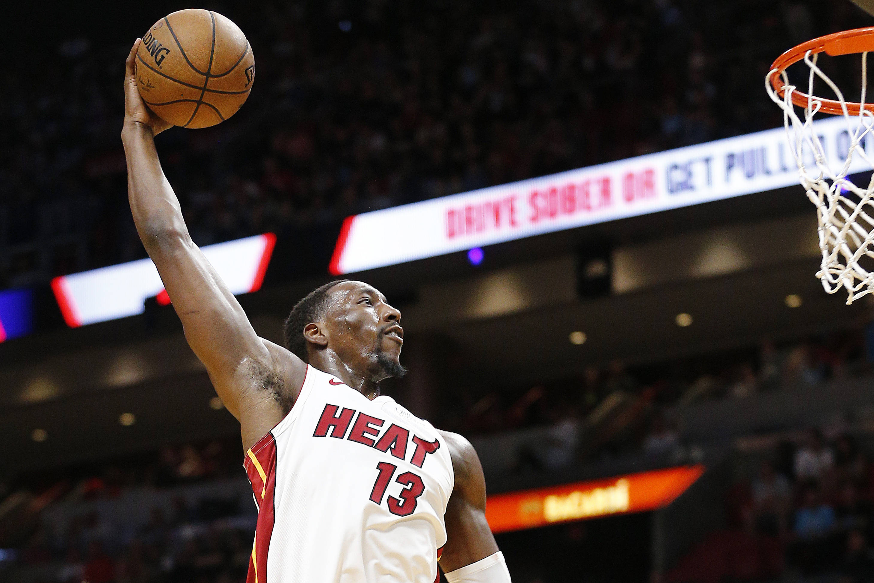 Bam Adebayo 火力灌籃特寫 壁紙 — 一位邁阿密熱火籃球運動員在燈光明亮的場館中高高躍起，進行強力入樽，觀眾模糊不清。