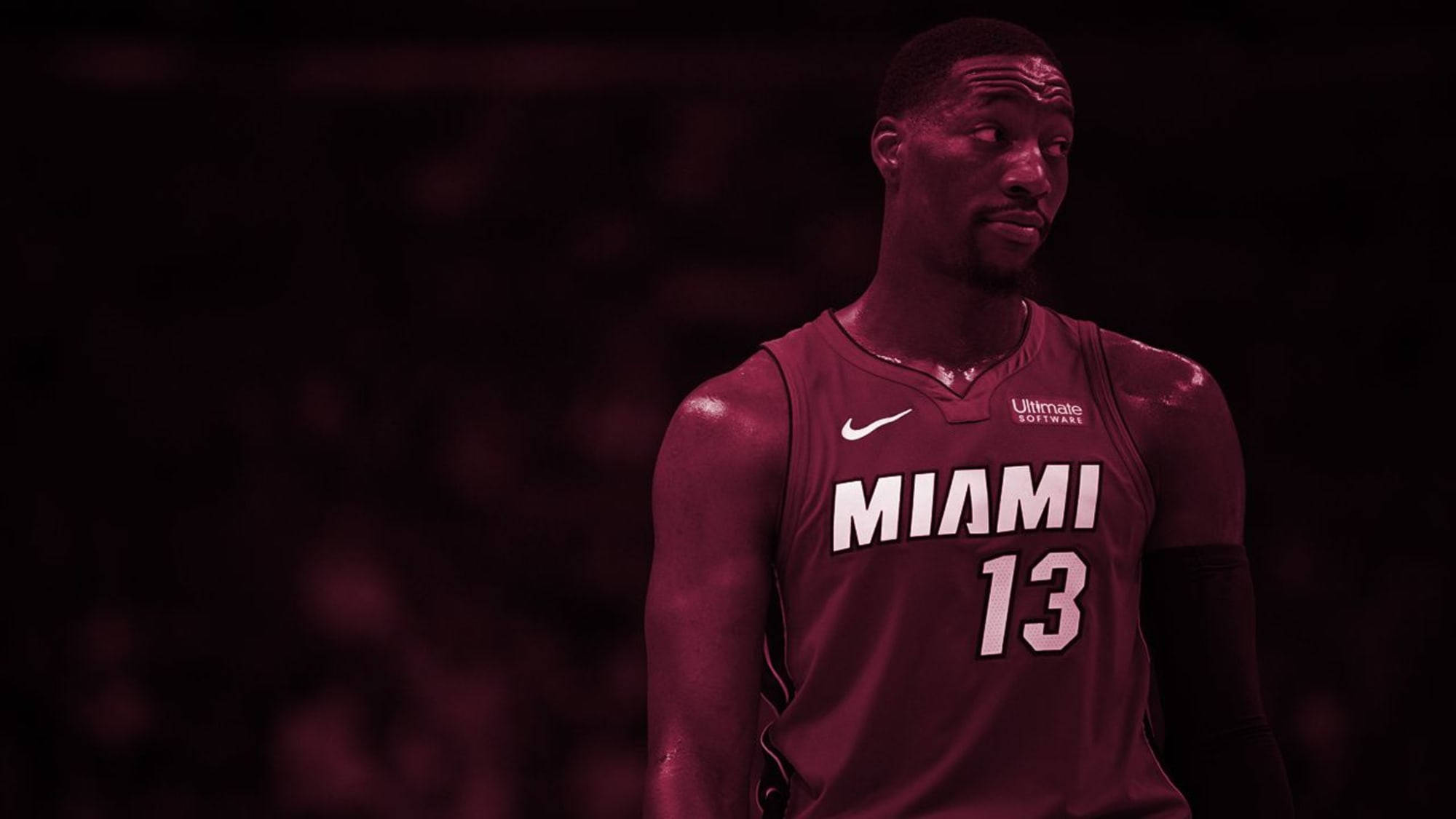 Bam Adebayo 紅色美學 壁紙 — 一名身穿栗色邁阿密球衣、號碼13的籃球運動員在昏暗的場館燈光下專注地站立。