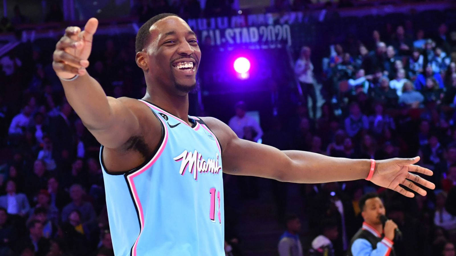Bam Adebayo 開心神情 壁紙 — 一位微笑的籃球運動員身穿淺藍色邁阿密球衣，在場館燈光下張開雙臂慶祝。