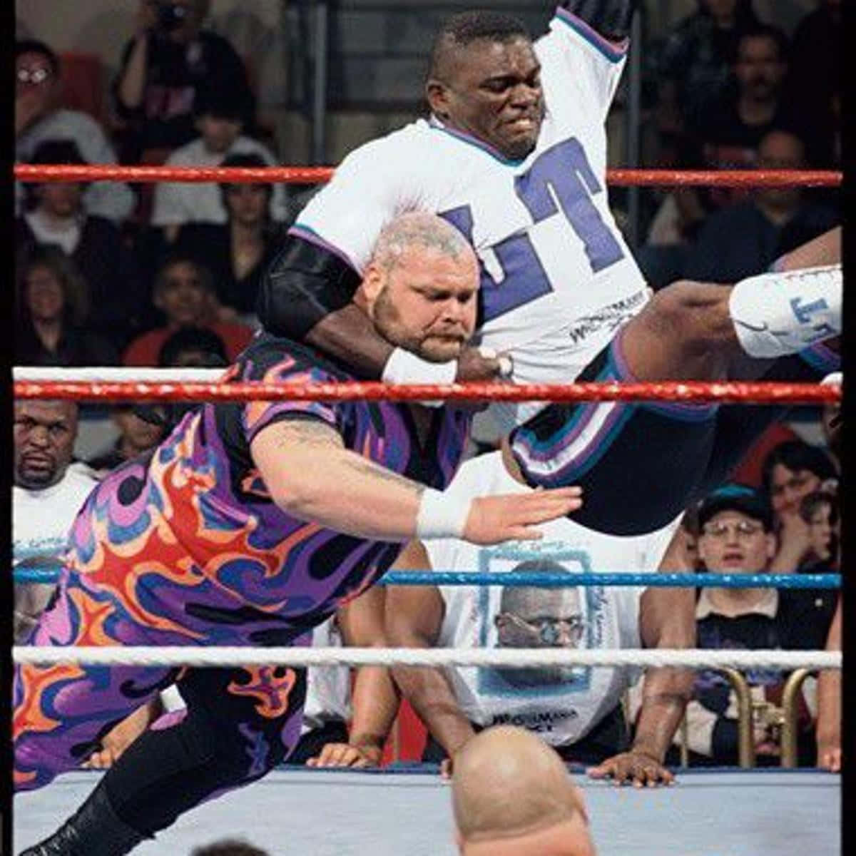 Bam Bam Bigelow 對戰 Lawrence Taylor 壁紙 — 兩名摔角手在擂台上交鋒，一人將另一人舉起，在觀眾的歡呼聲中施展高衝擊力招式。