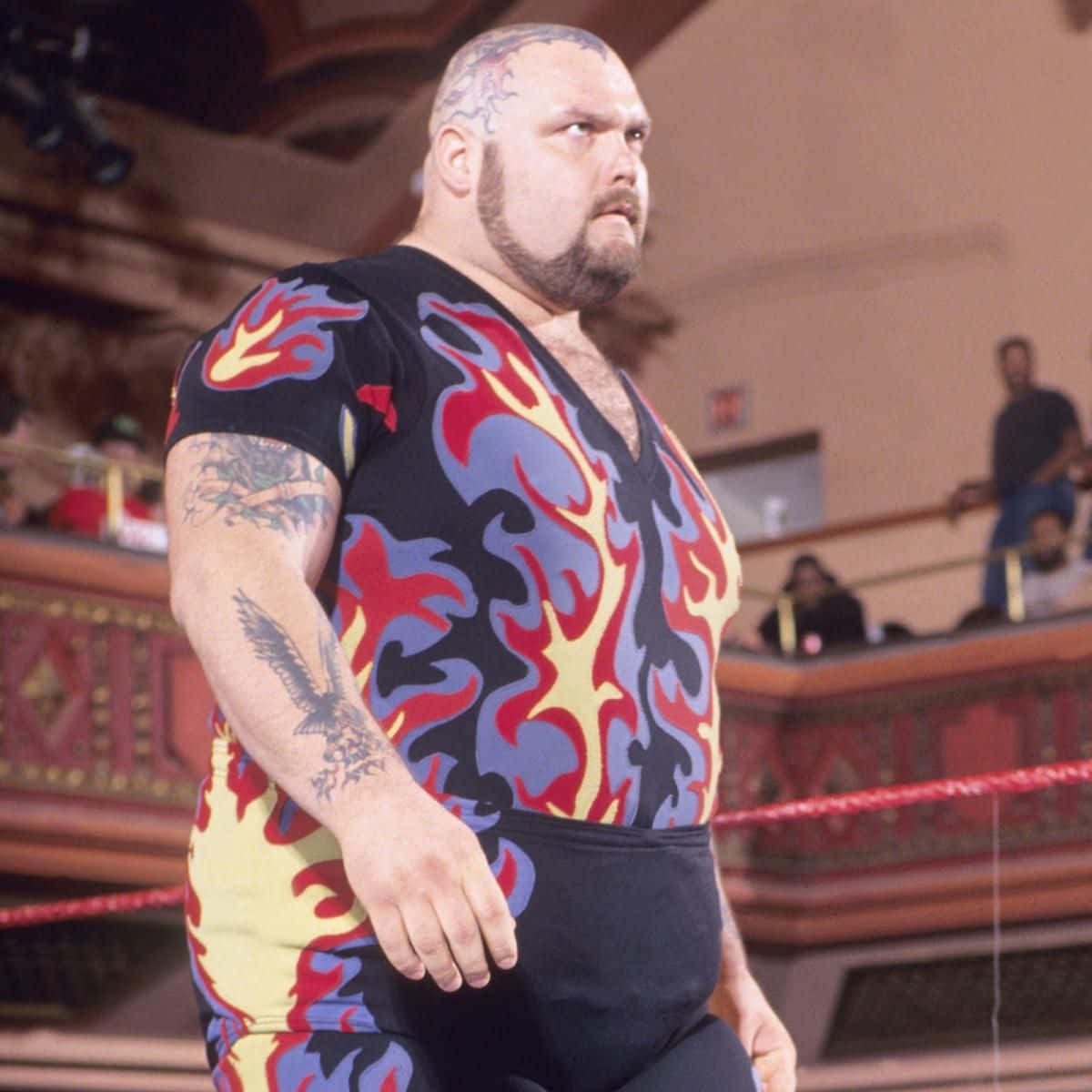Bam Bam Bigelow 2015 WWE Heritage Wrestling 嚴肅造型 壁紙 — 一位肌肉發達的摔角手穿著火焰圖案緊身衣，帶有紋身和光頭，站在擂台上。