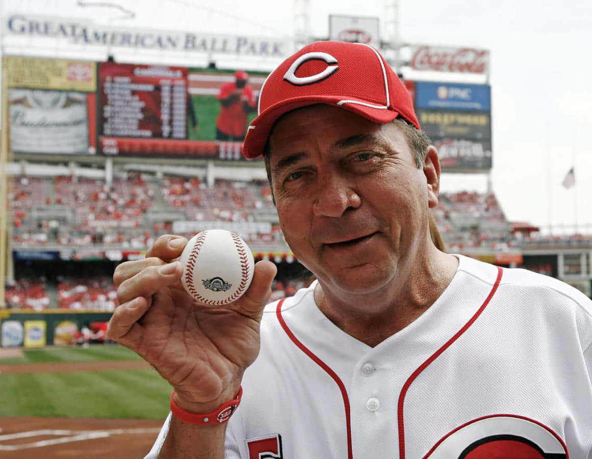  壁紙 — 一位戴紅色帽、穿白色球衣的棒球運動員在Great American Ball Park微笑著拿著棒球。