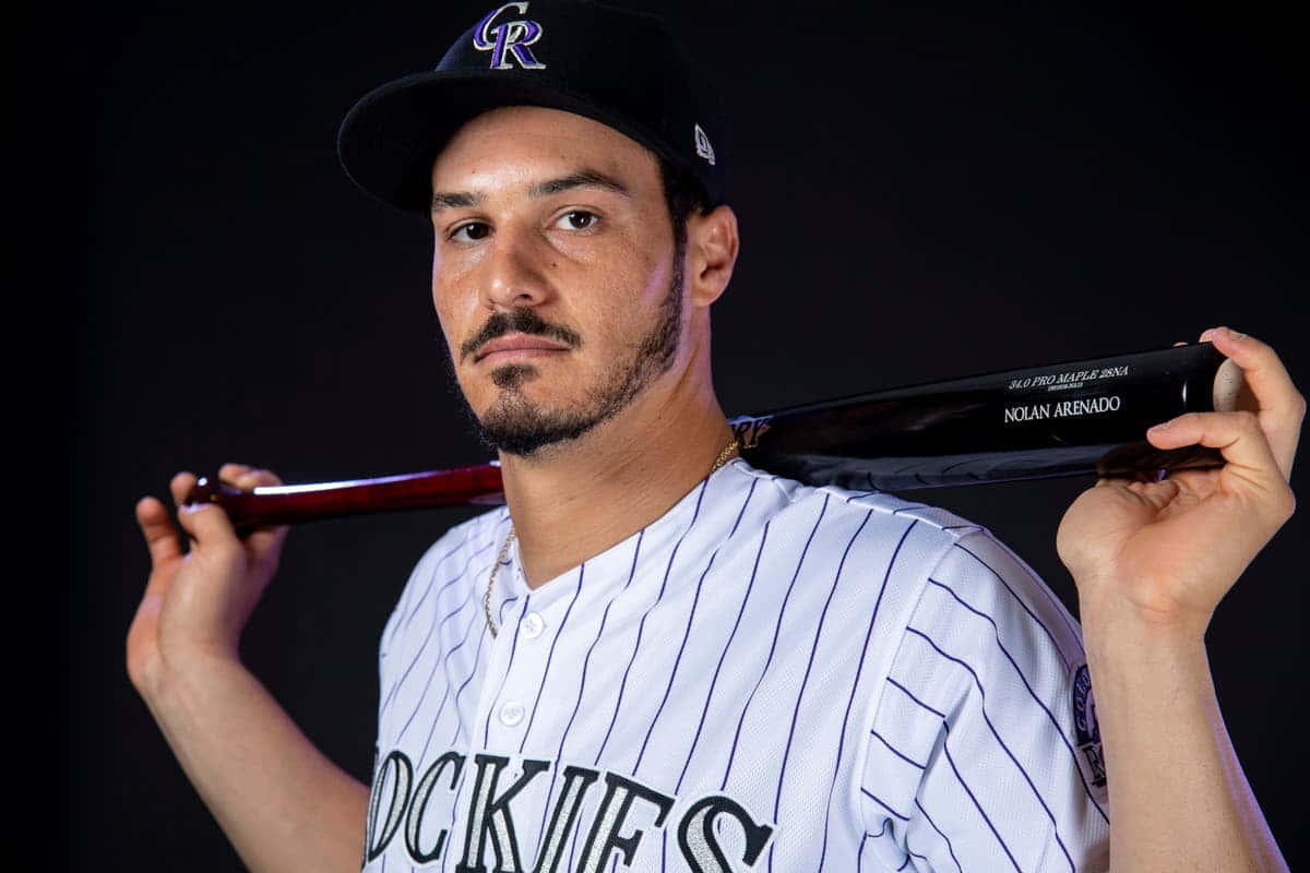  壁紙 — 棒球運動員 Nolan Arenado 身穿洛磯隊制服，在深色工作室背景中將球棒扛在肩上。