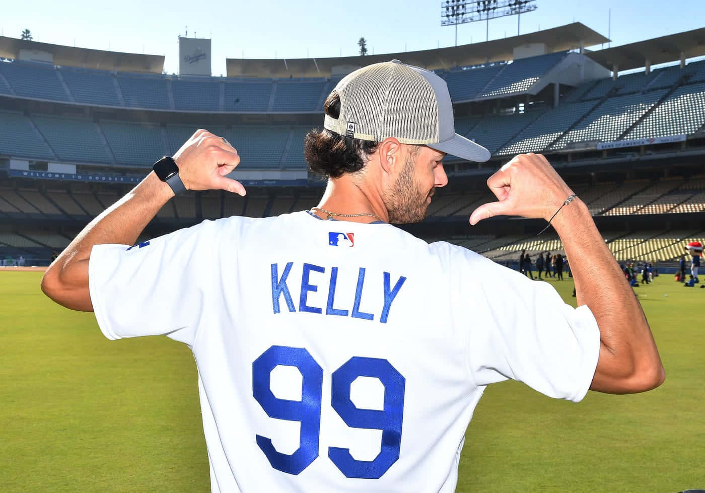  壁紙 — 一名身穿白色球衣、印有藍色「KELLY 99」的棒球運動員，在陽光明媚的球場上彎曲雙臂。