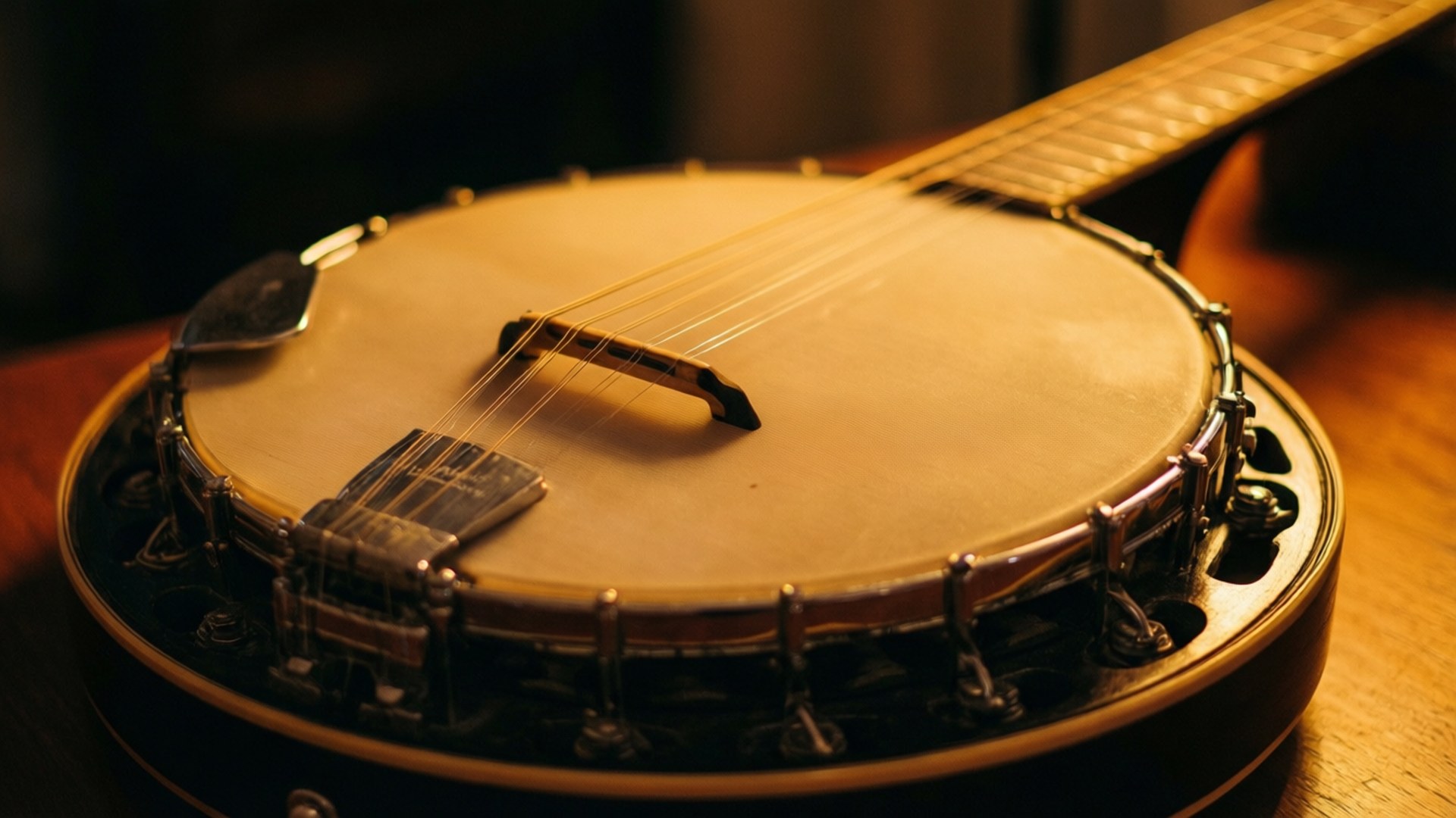 A wooden banjo with metal hardware resting on a wooden table. 壁紙