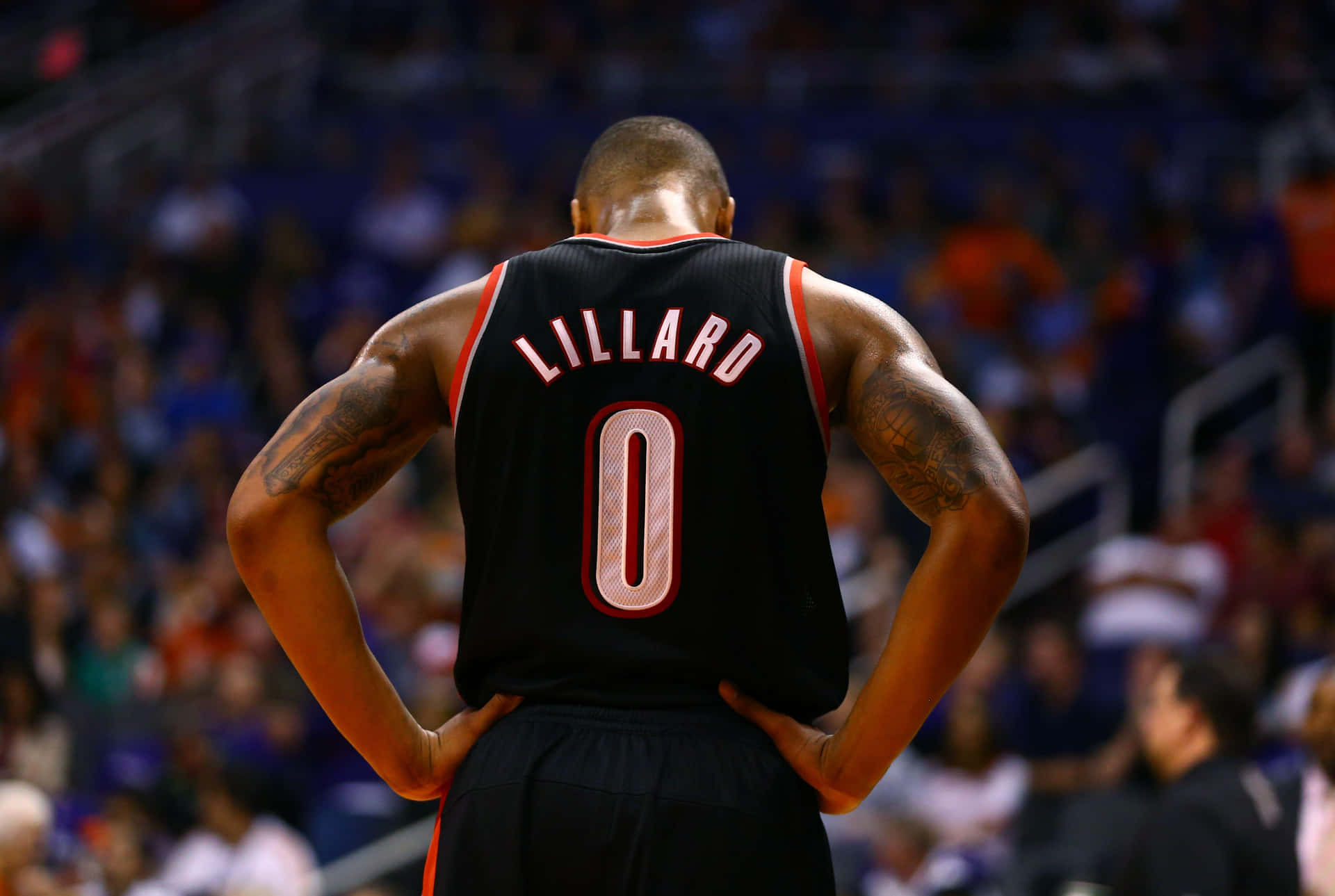  壁紙 — 一名身穿黑色Lillard 0球衣的籃球運動員，雙手叉腰，面向場館內模糊的人群。