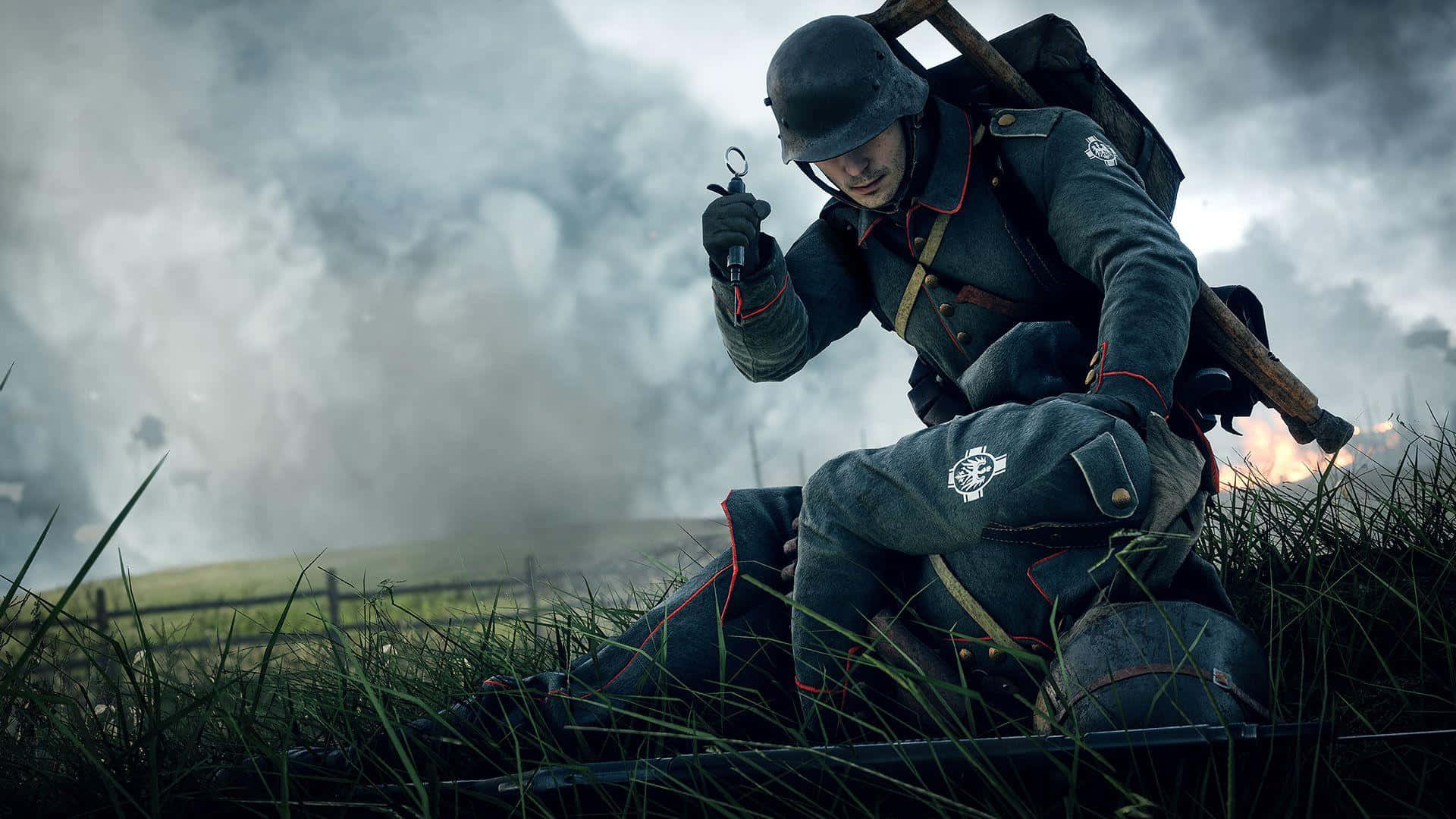 《Battlefield V》醫療兵背景 壁紙 — 一名身穿灰色軍裝的士兵蹲在草地上，手持手榴彈，身後煙霧瀰漫，天空多雲。