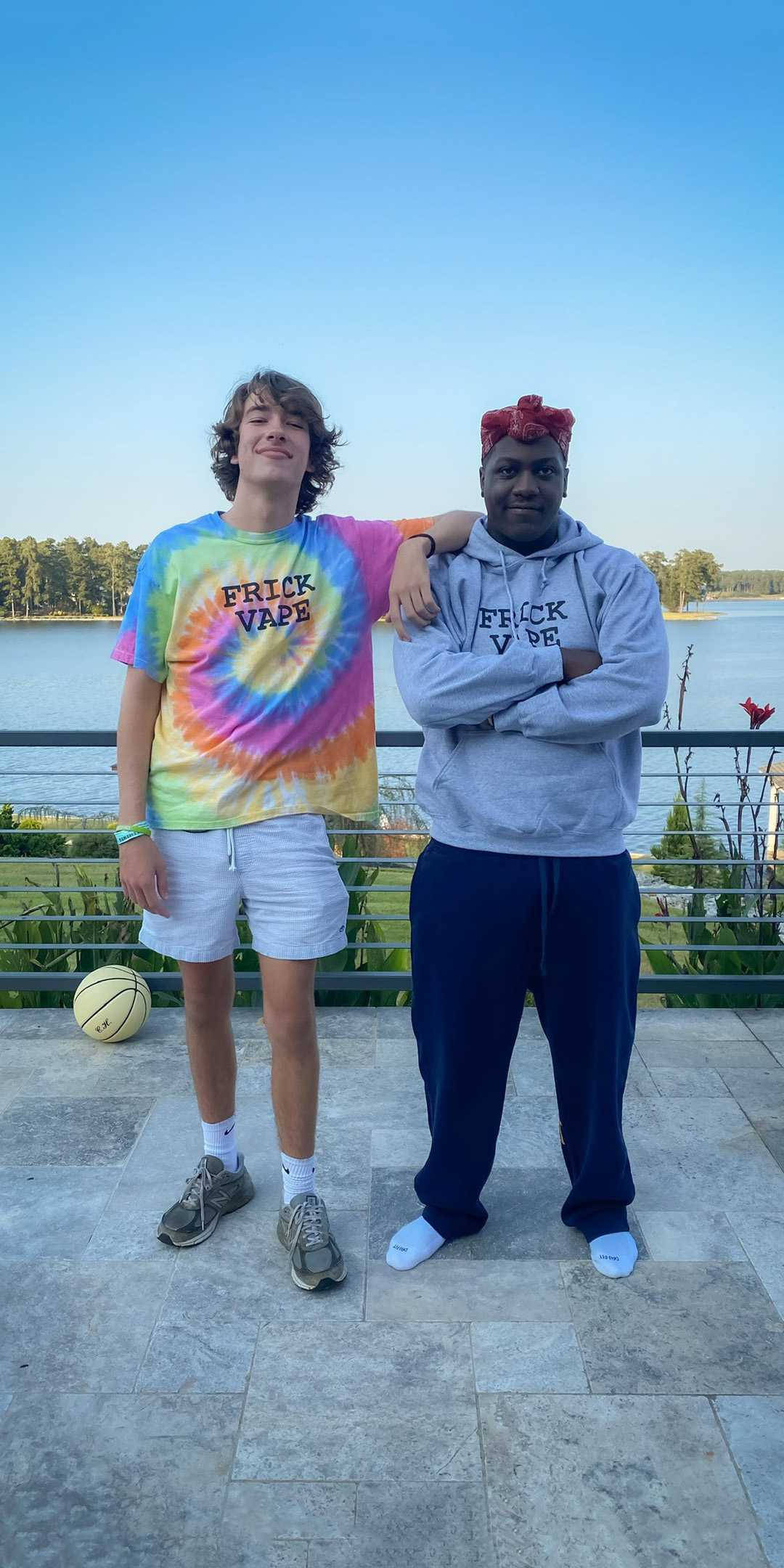 Baylen Levine 與歌手Lil Yachty 壁紙 — 兩名年輕男子在瓷磚陽台上隨意擺姿勢，俯瞰著平靜的湖泊，湖邊有樹木，天空清澈湛藍。
