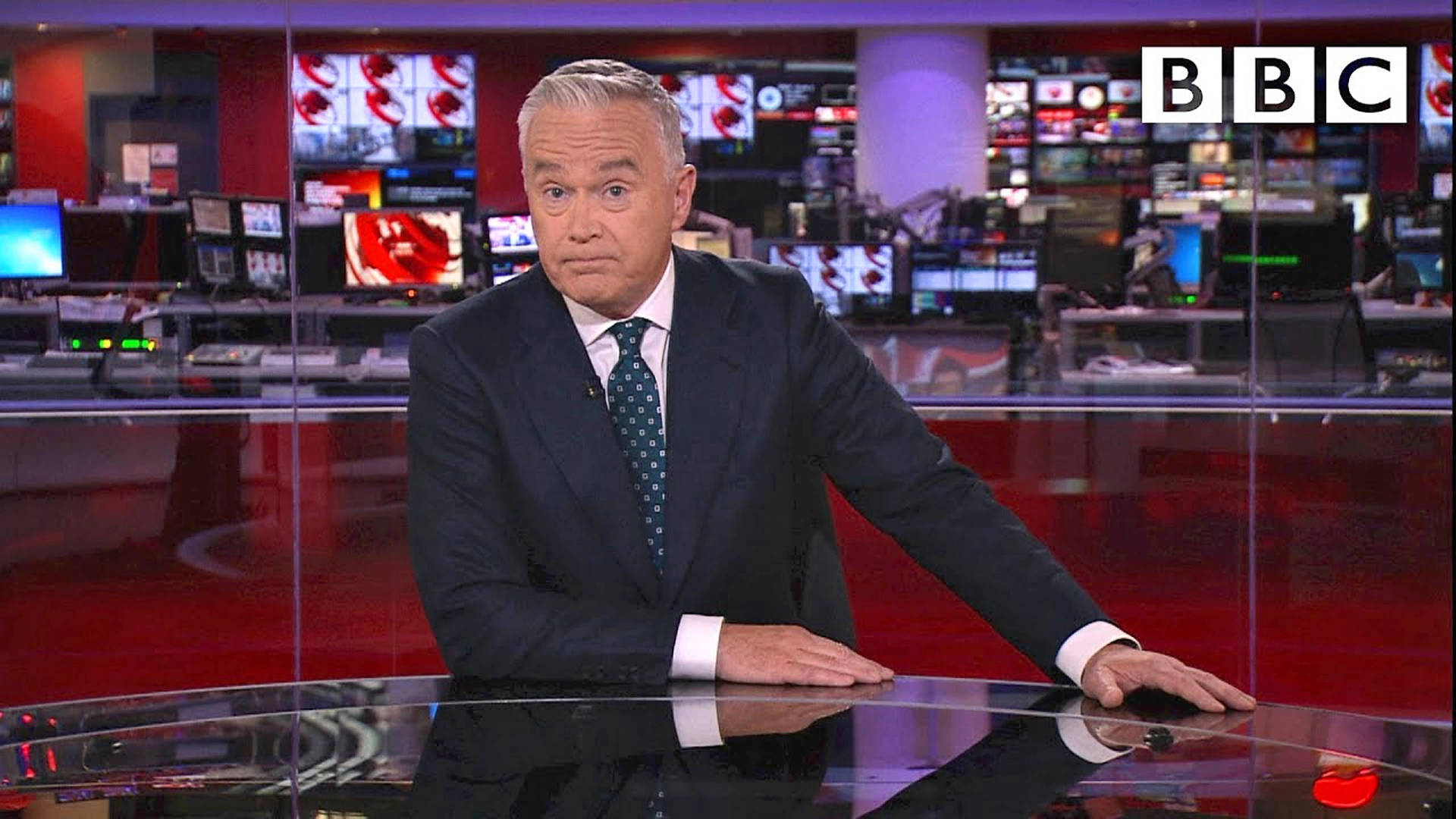 BBC新聞主播在現代廣播錄影棚的紅色桌子前。
