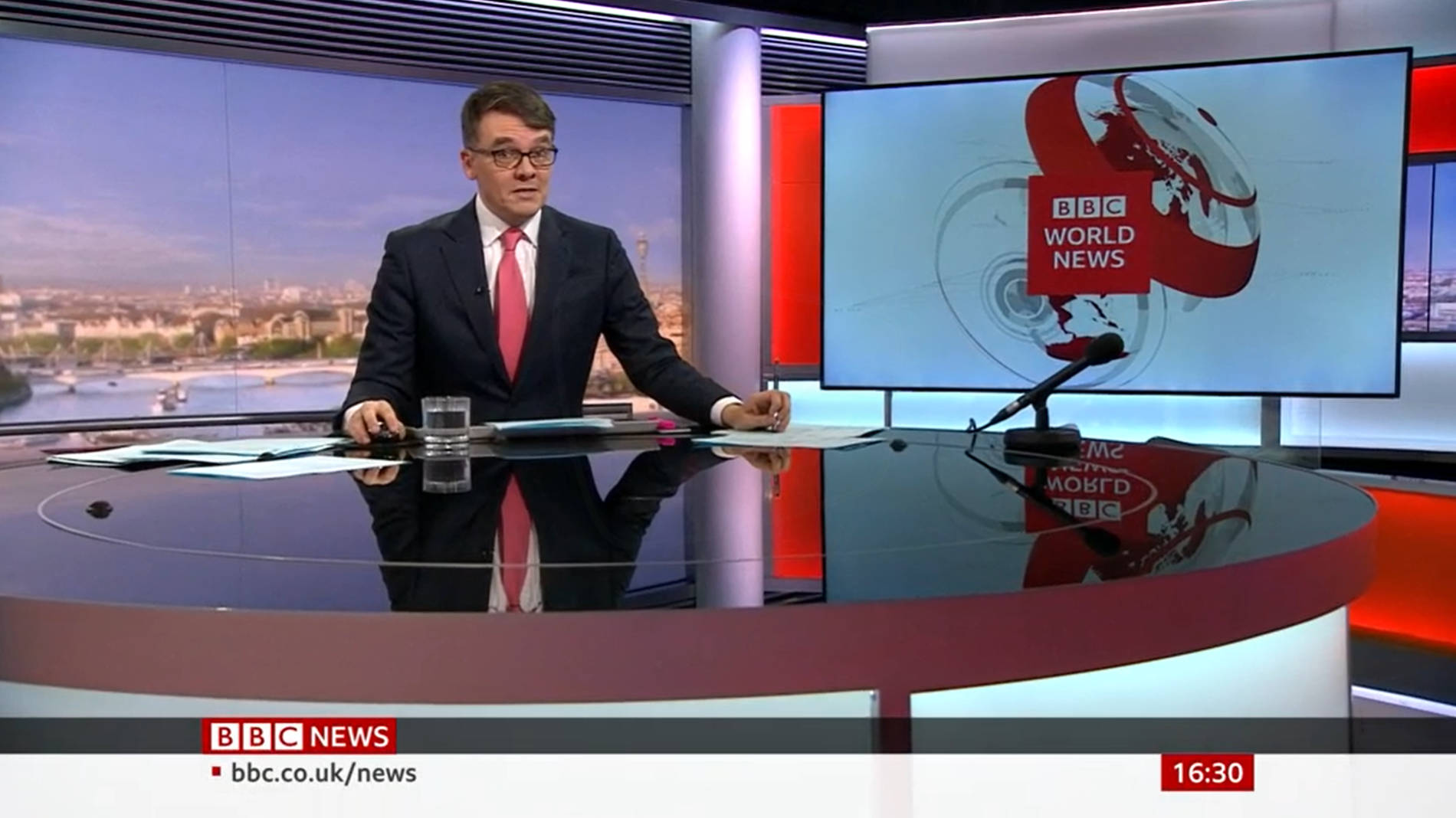 BBC世界新聞主播在現代演播室桌前，背景有城市景觀和標誌屏幕。
