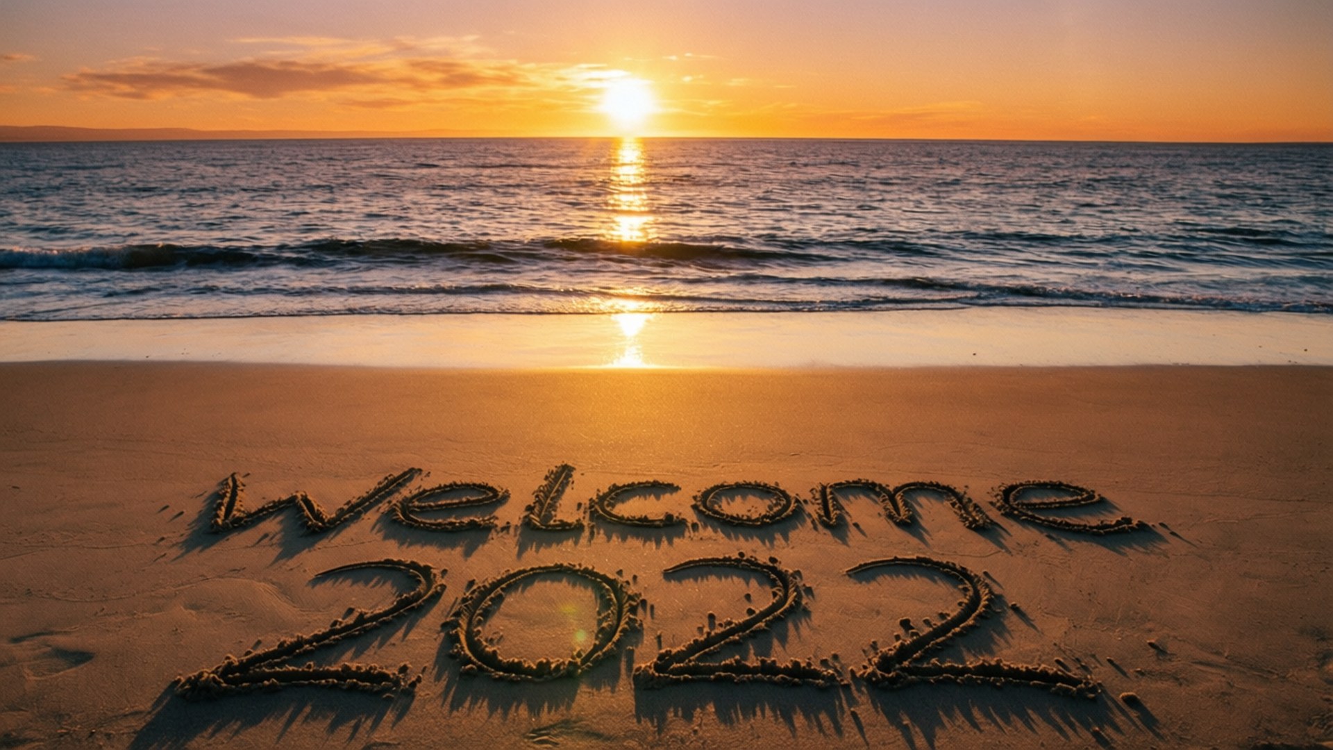 海洋上的日落，水邊沙灘上寫著「Welcome 2022」
