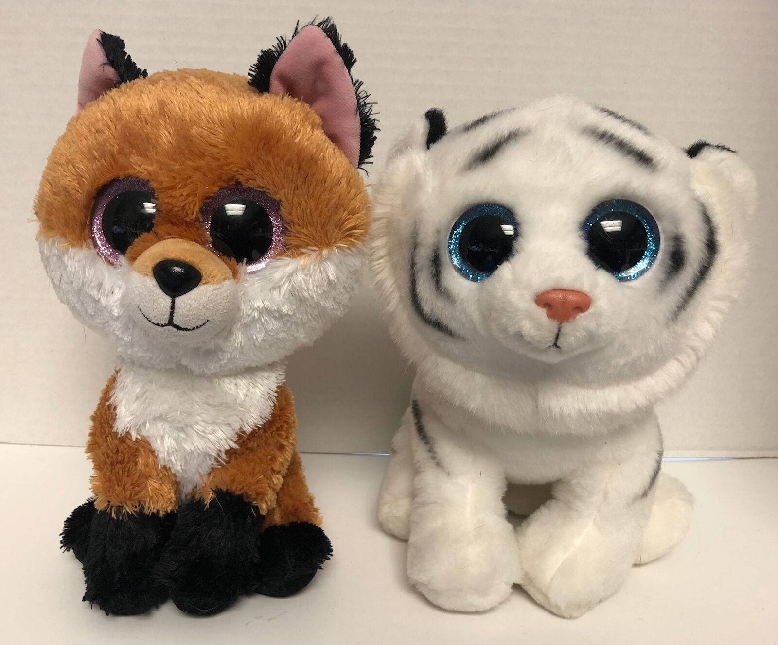 Beanie Boos狐狸與白虎 壁紙 — 兩個毛絨玩具，一隻狐狸和一隻白老虎，眼睛閃閃發光，並排坐在平坦的表面上。