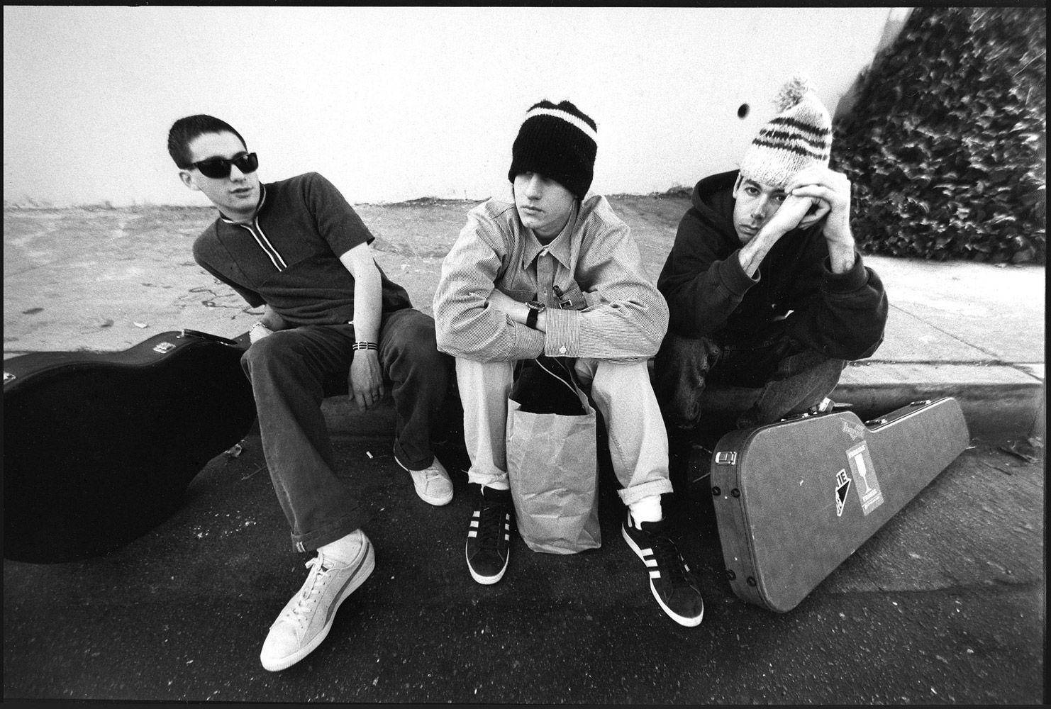 Beastie Boys《Check Your Head》專輯封面 壁紙 — 三位年輕男子穿著休閒街頭服飾坐在行人路上，旁邊放著結他盒，一張粗糙的黑白照片。