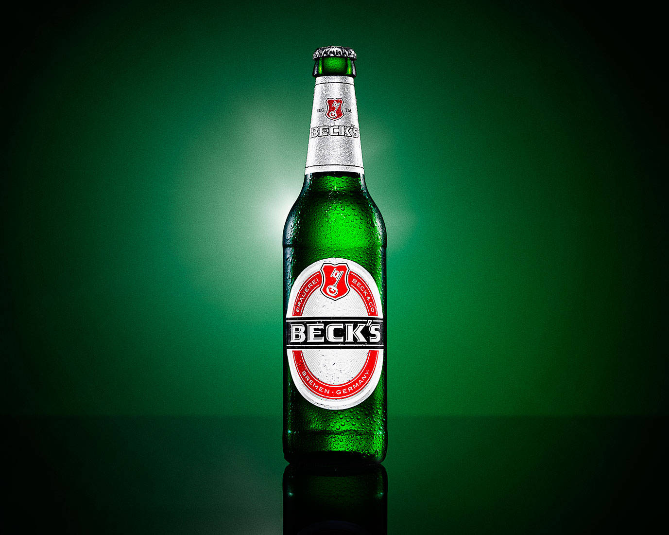 冰凍的 Beck's 啤酒瓶在深綠色反光表面上凝結水珠。