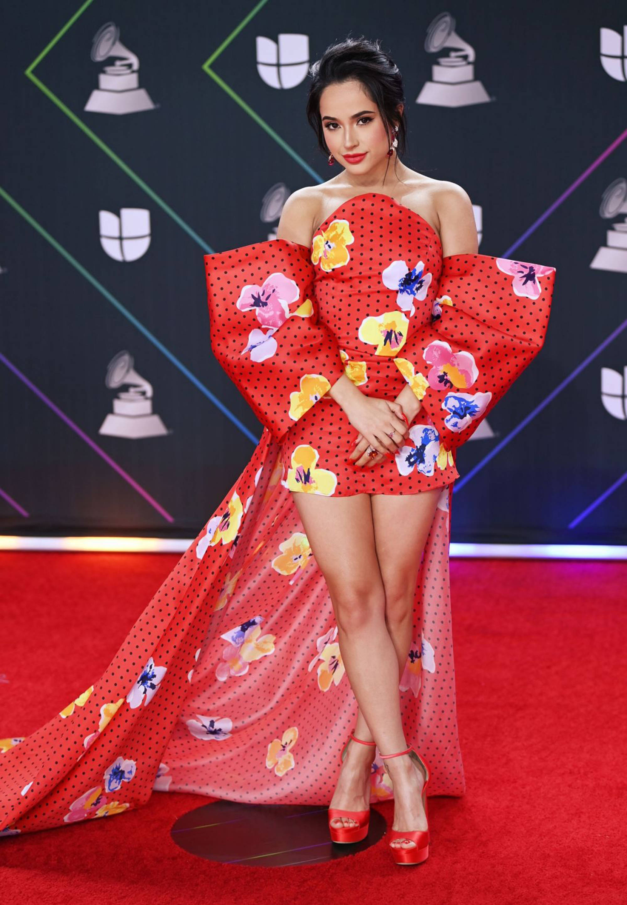 Becky G 22 屆拉丁音樂獎登台演出 壁紙 — 一位身穿大膽紅色花卉禮服、搭配戲劇性袖子的女性，在格林美獎活動的紅地毯上自信地擺姿勢。