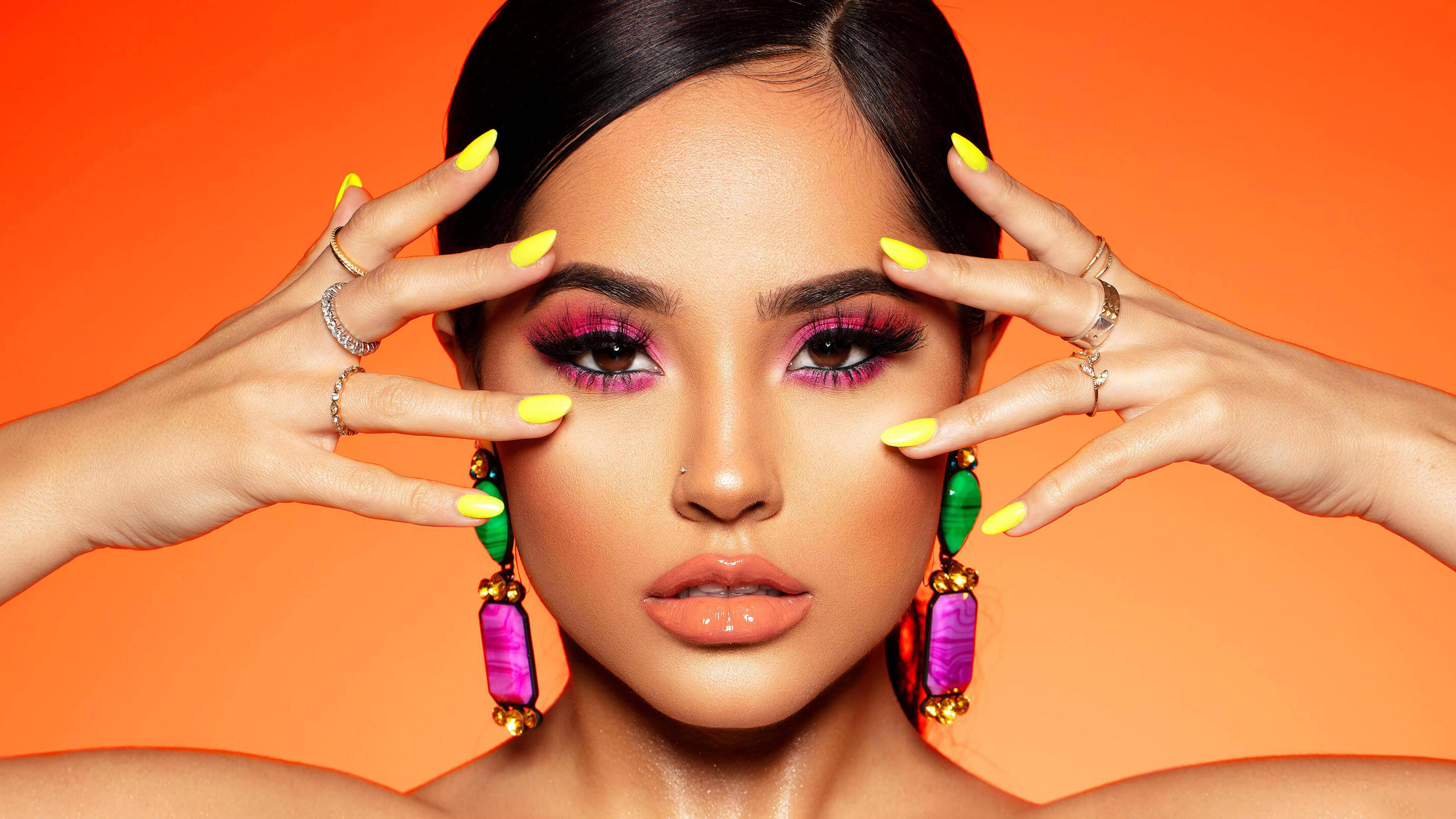 Becky G 展現招牌 Rosa 風格 壁紙 — 一位女士以大膽的粉紅色眼影和螢光黃色指甲，在充滿活力的橙色背景前襯托她的臉龐。
