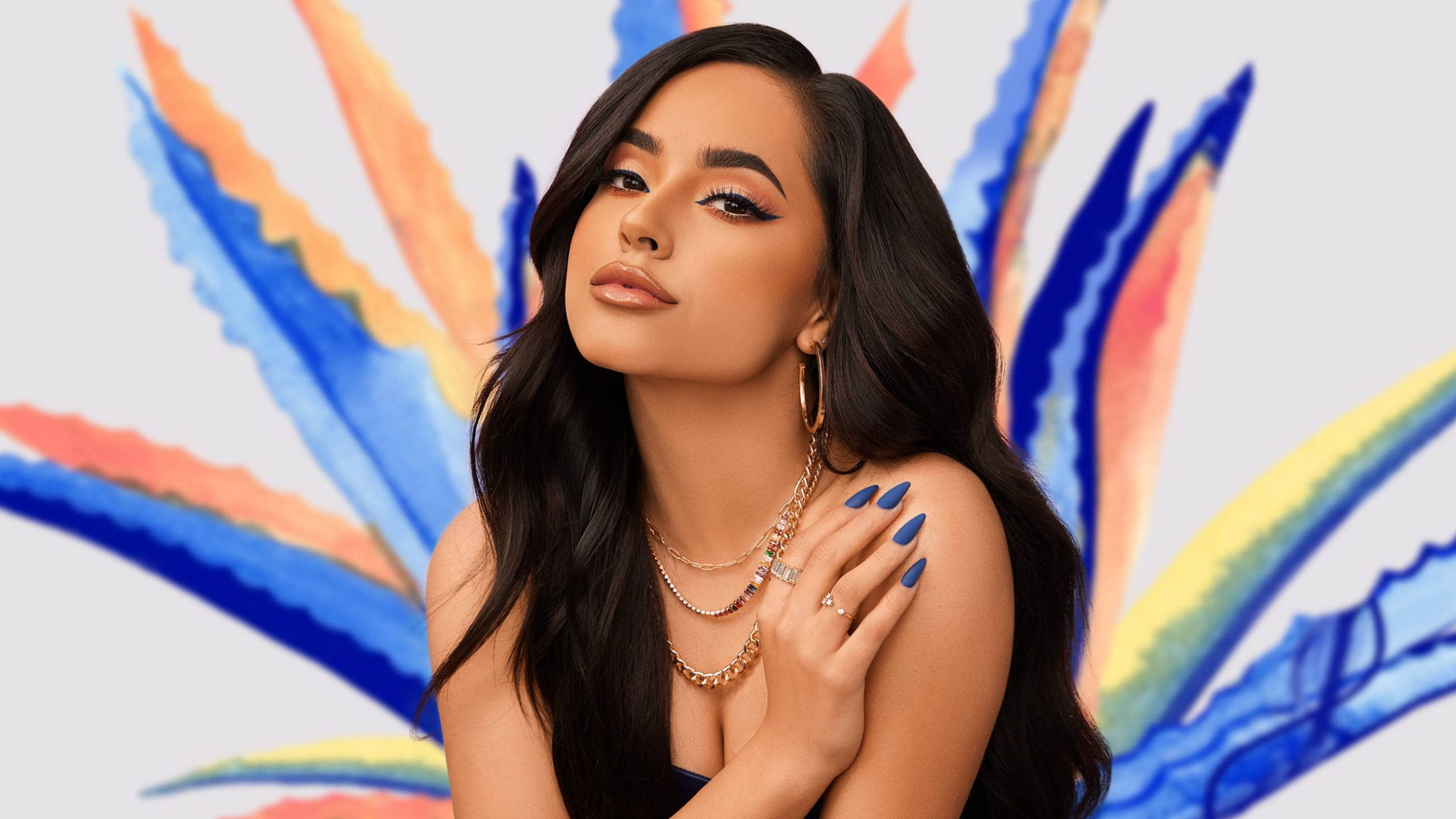 Becky G 為 Treslúce Beauty 品牌拍攝 壁紙 — 一位擁有長長黑髮和藍色指甲的女性，在藍色、橙色和黃色筆觸的鮮豔抽象背景前優雅地擺姿勢。