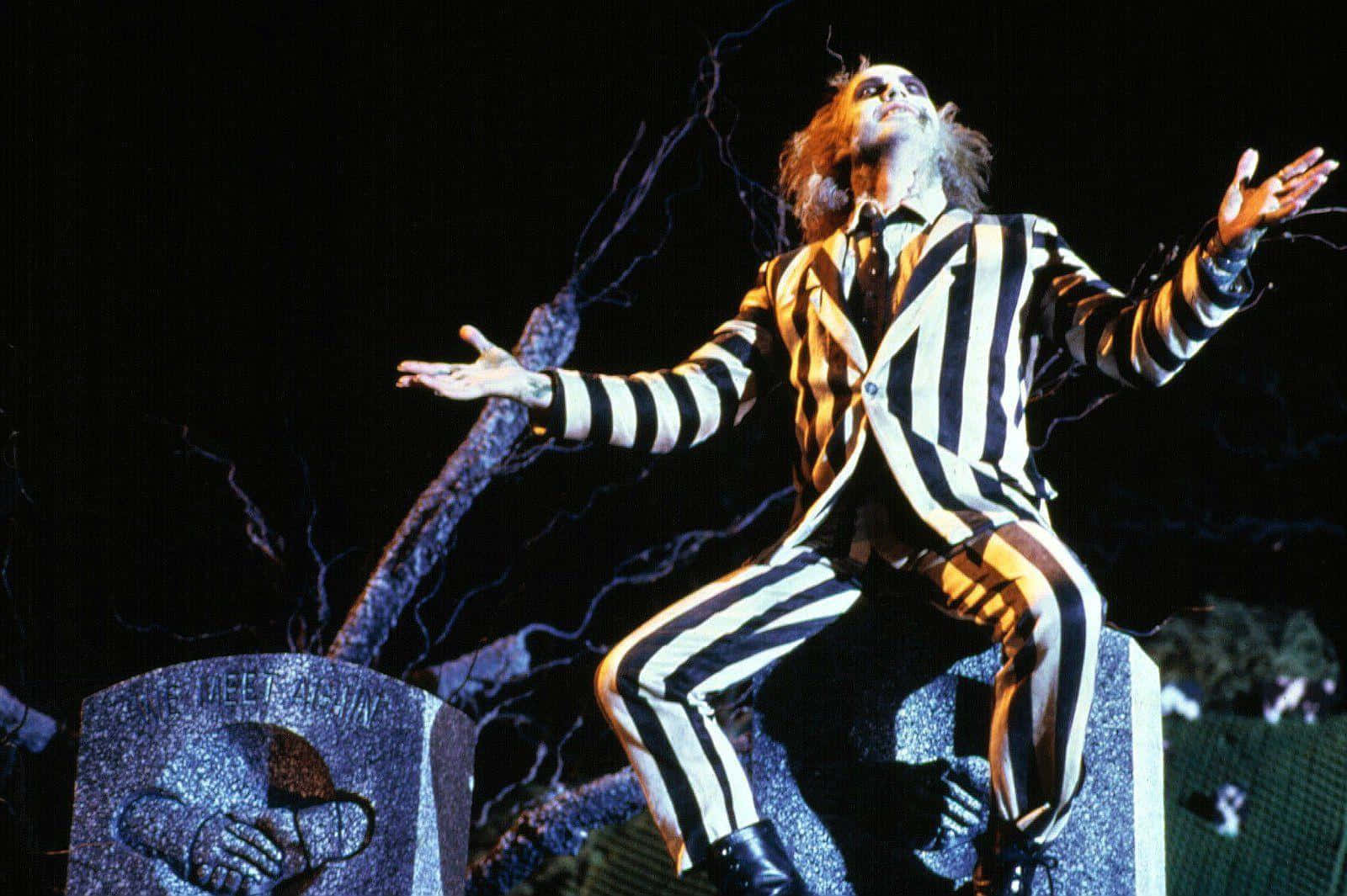 Beetlejuice 桌布 壁紙 — Beetlejuice 穿著其標誌性的條紋西裝坐在墓碑上，閃電在他周圍劈啪作響，背景是黑暗的夜空。