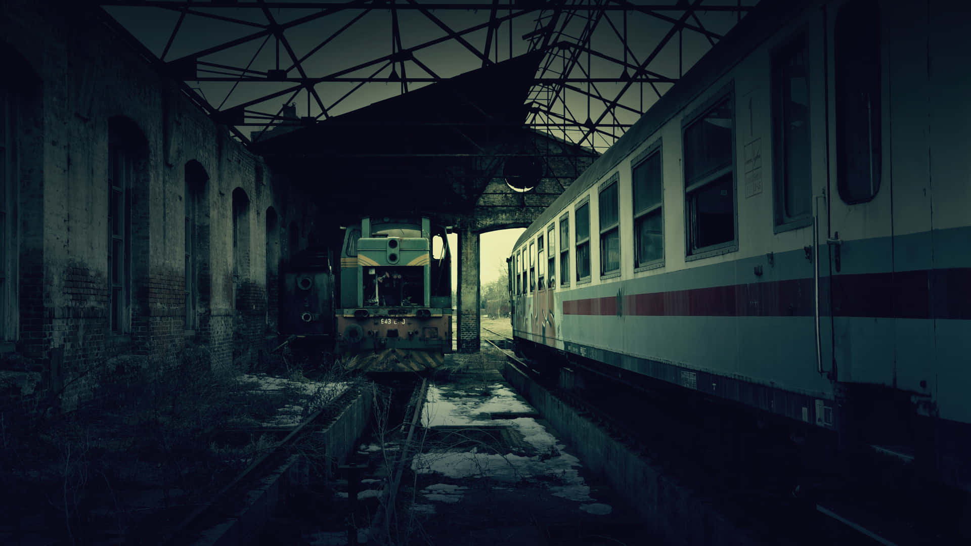  壁紙 — 被遺棄的火車在破舊的車站屋頂下靜止不動，微弱的暮色中雪花灑落在路軌上。