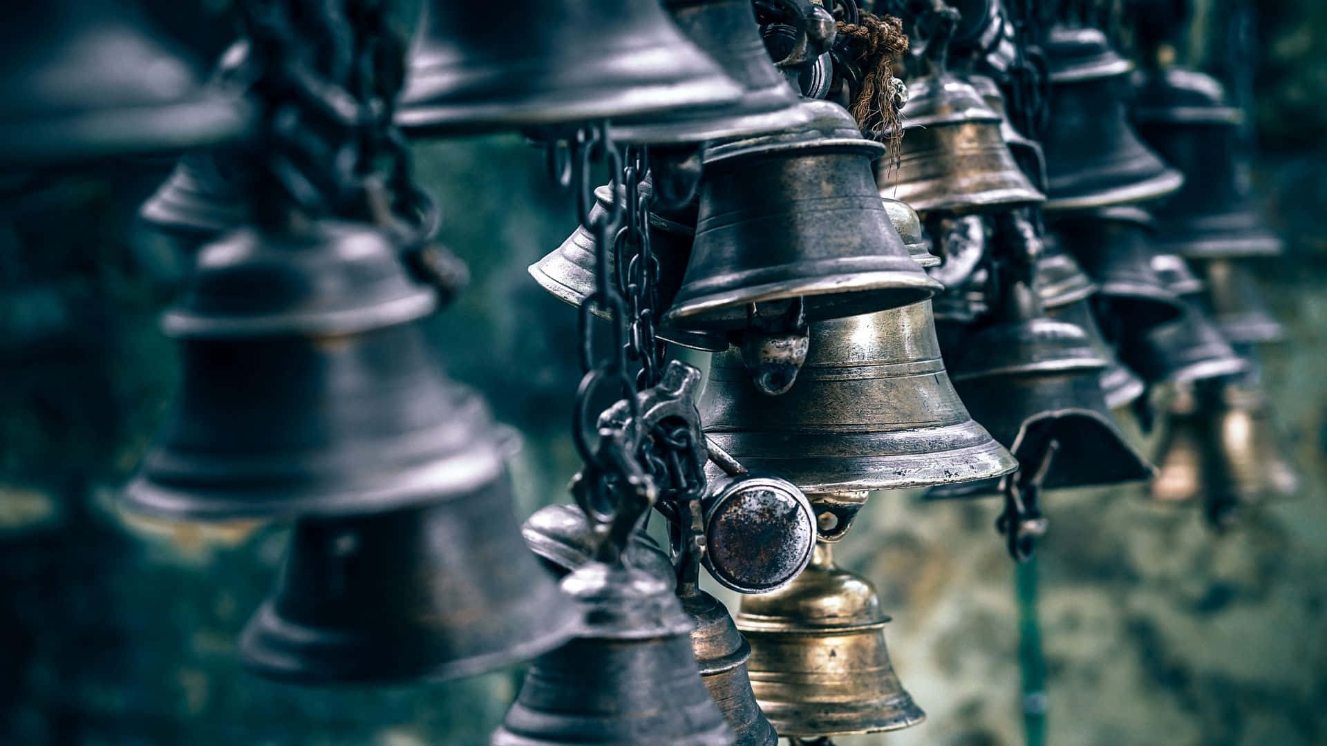 Bell — 聽見差異 壁紙 — 一簇風化的金屬鐘用鏈條懸掛在模糊的綠色背景上。