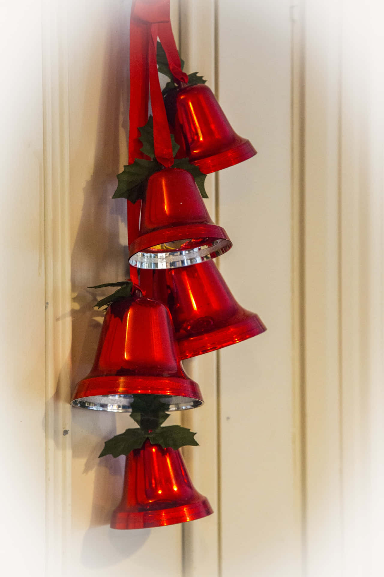 Bell — 開啟潛力之門 壁紙 — 四個閃亮的紅色節日鈴鐺裝飾著冬青葉，像瀑布一樣掛在淺色木門上。