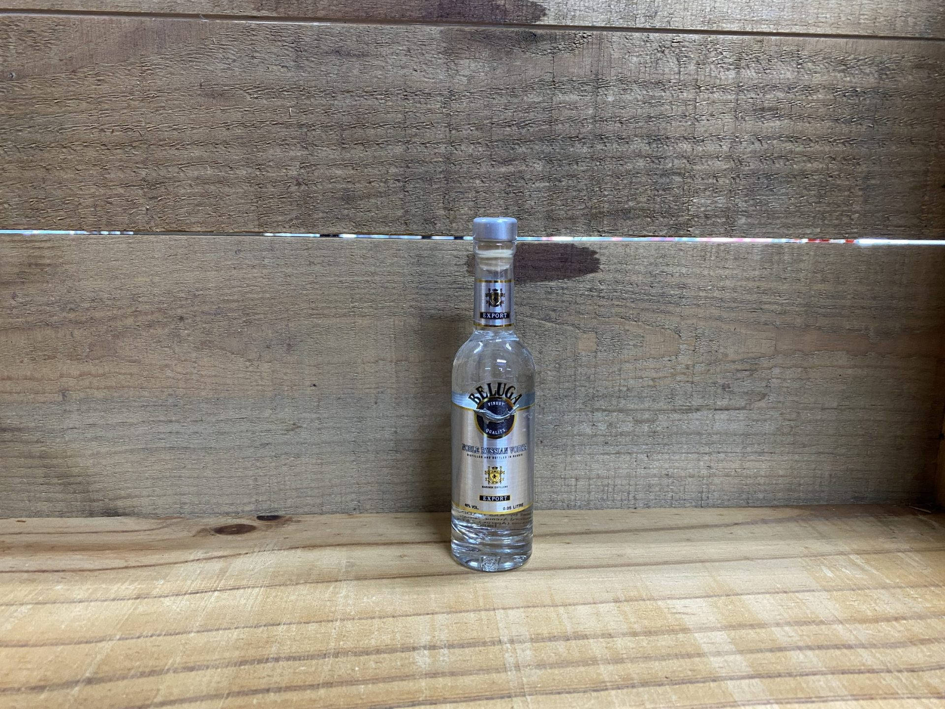 一個透明的Beluga伏特加酒瓶放在木架上，背景是木牆。