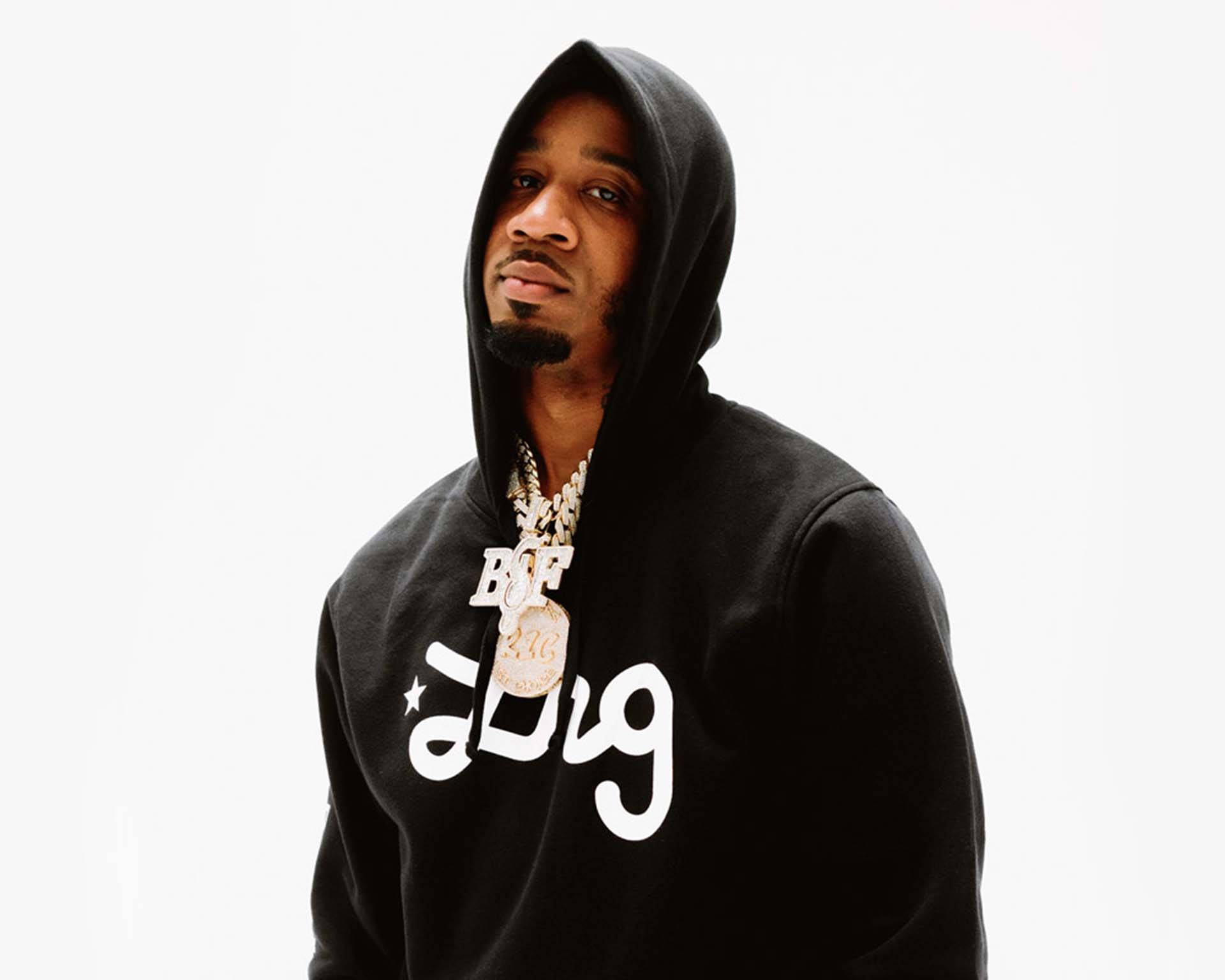 Benny The Butcher 穿 LRG 套裝 壁紙 — 一名身穿黑色連帽衫（帶白色標誌）和金色鏈條的男子在純白色背景前擺姿勢。