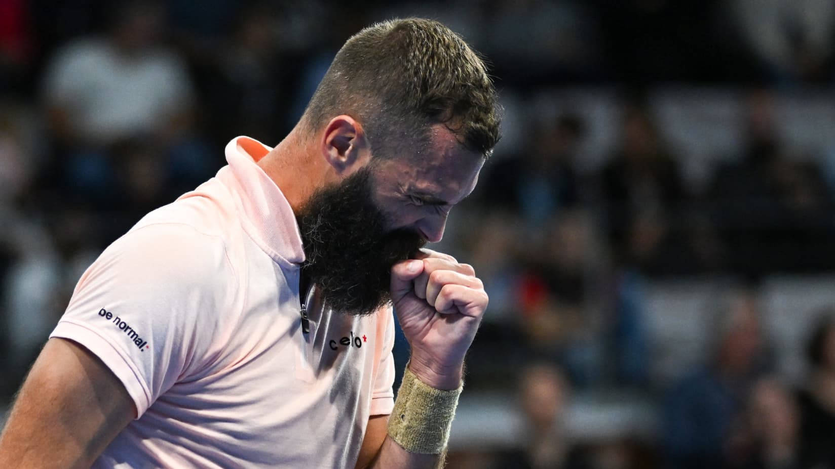 Benoit Paire 低頭握拳慶祝 壁紙 — 一位留鬍鬚的網球運動員穿著淺粉紅色襯衫，在比賽中情緒激動的時刻將拳頭握在嘴邊。