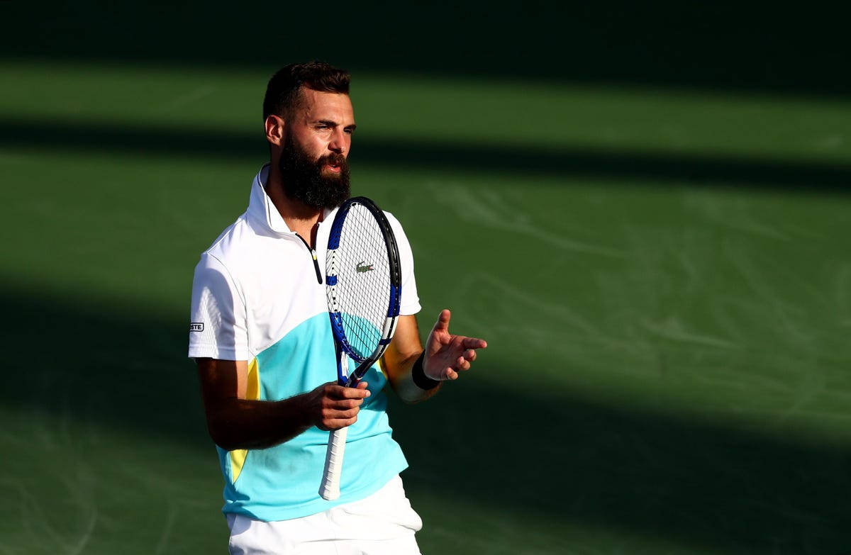 Benoit Paire 在綠地場上談話 壁紙 — 一位留鬍鬚的網球選手，身穿白色和青綠色襯衫，在陽光明媚的綠色球場上拿著球拍做手勢。