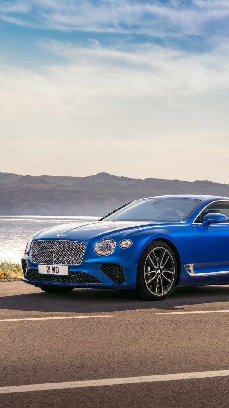 藍色 Bentley 跑車停泊在海邊道路上，背後有山脈和海洋。