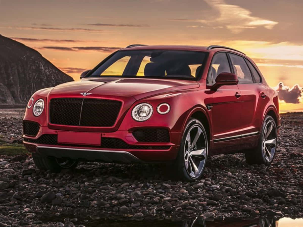 奢華與冒險 — 隨心所欲駕馭Bentley Continental 壁紙 — 一架亮紅色Bentley Bentayga SUV停泊在岩石海灘上，背景是日落時分的山脈。