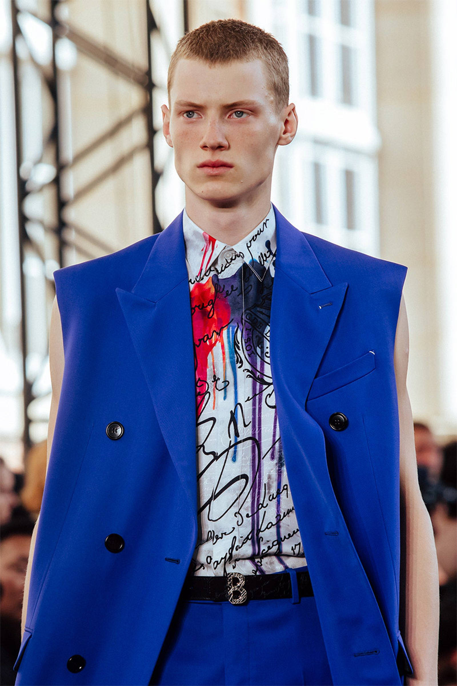 Berluti 2020春季系列 壁紙 — 一位男模特兒在時裝秀上自信地穿著一件大膽的藍色無袖西裝，內搭塗鴉風格襯衫。