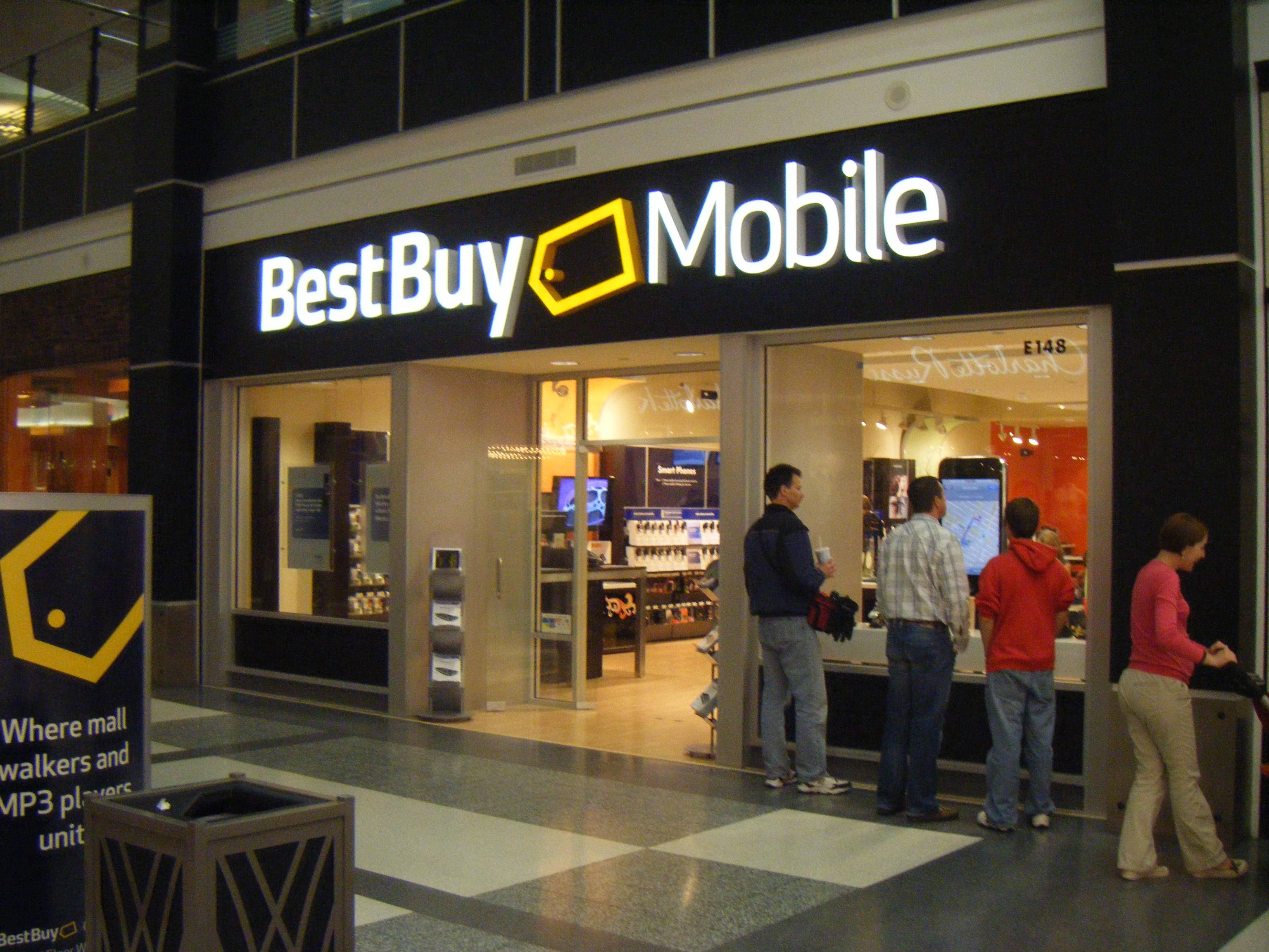 Best Buy移動商場店 壁紙 — 購物者聚集在一個光線明亮的Best Buy Mobile商店外，商場內有棋盤格地板和玻璃門。