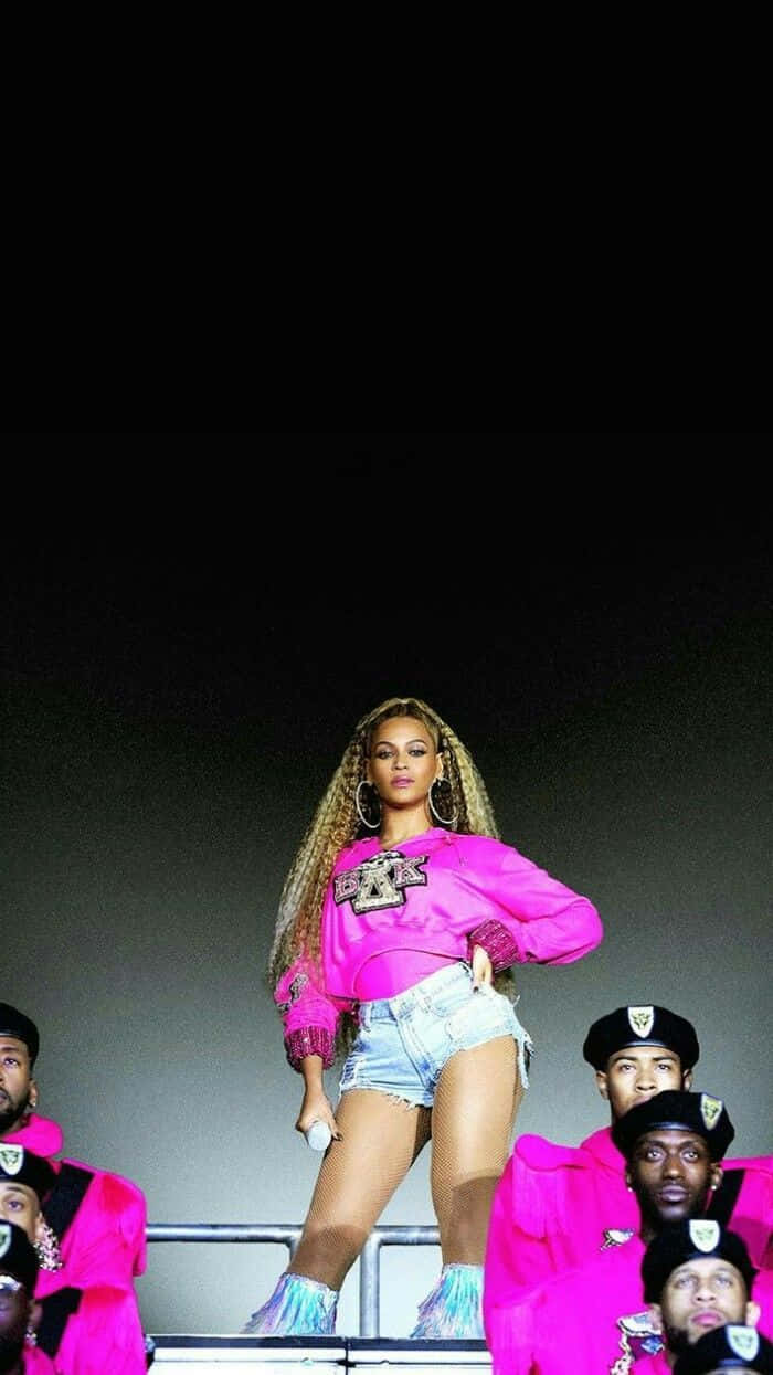 Beyoncé 桌布 壁紙 — Beyoncé 在明亮的演唱會燈光下，身穿鮮豔粉紅服裝，被身穿搭配服飾的舞者包圍，主宰舞台。