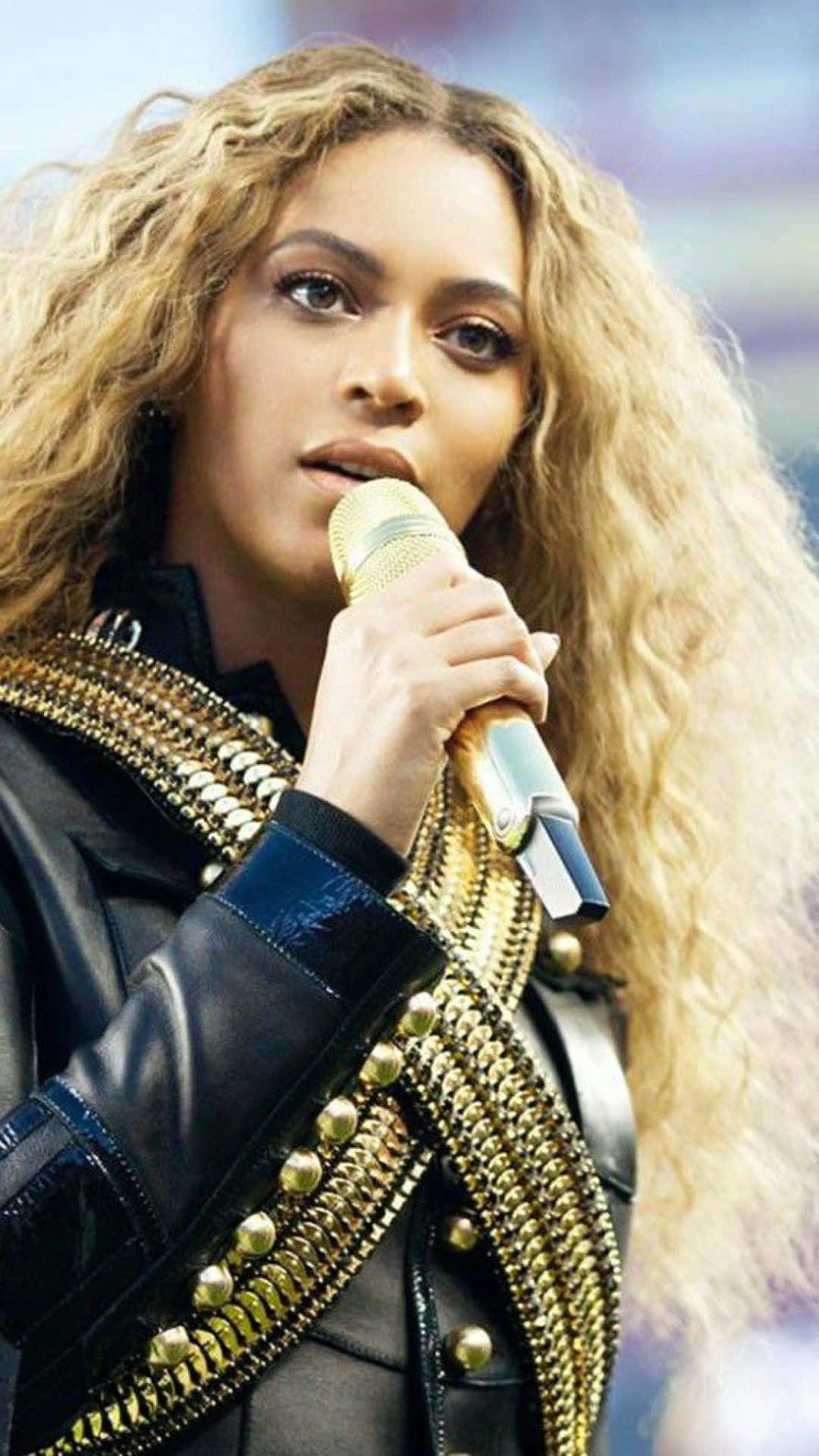 Beyoncé 桌布 壁紙 — Beyoncé 專注地表演，手持金色麥克風，身穿飾有金色鏈條的黑色皮褸。
