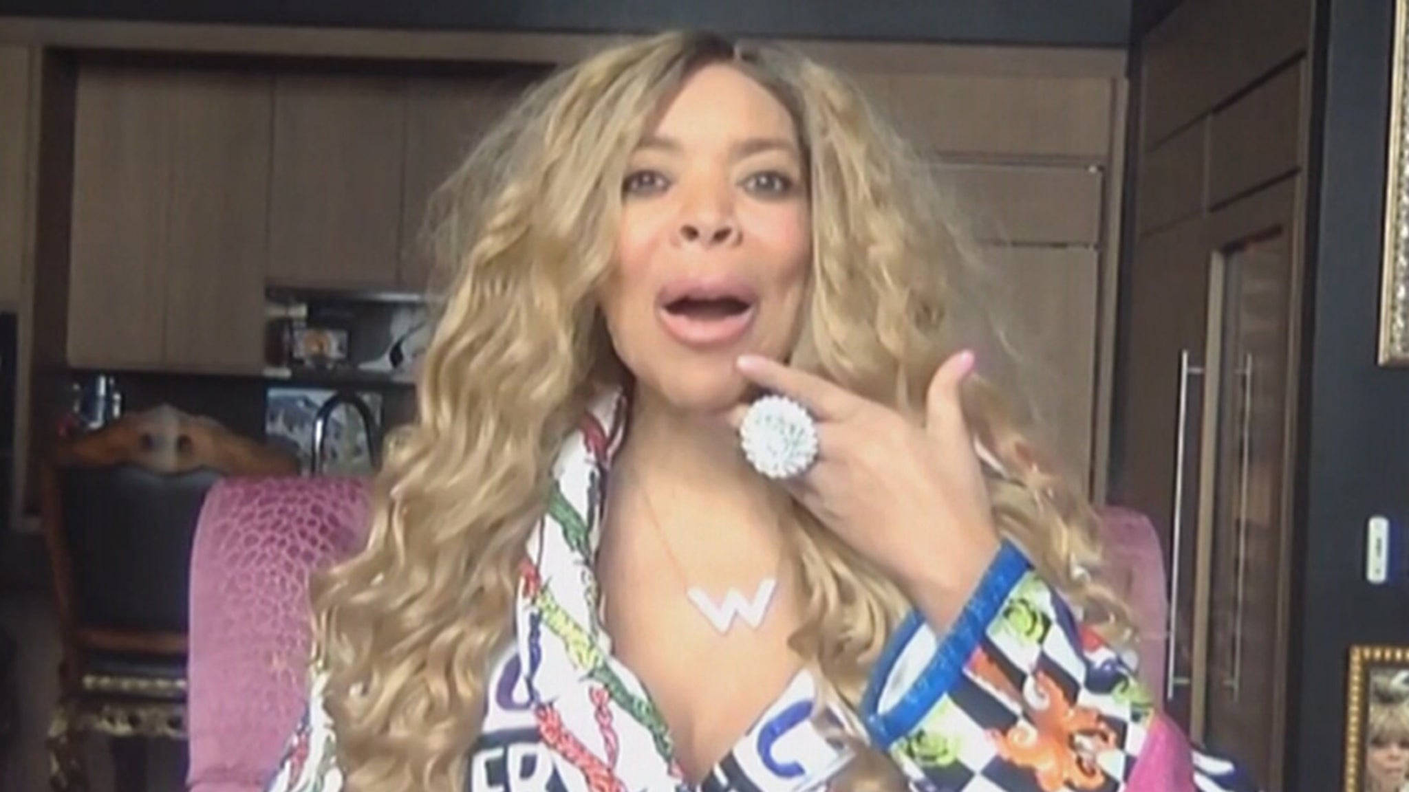 Wendy Williams Podcast 壁紙 — Beyoncé 留著長長的金色捲髮，戴著一個大戒指，坐在色彩繽紛的房間裡，俏皮地做手勢。