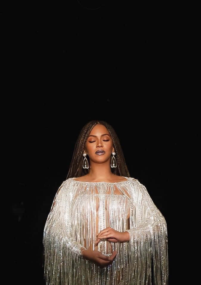 Beyoncé 桌布 壁紙 — Beyoncé 身穿閃閃發光的銀色流蘇長裙，在純黑背景前靜靜站立，閉上眼睛，陷入平靜的沉思。