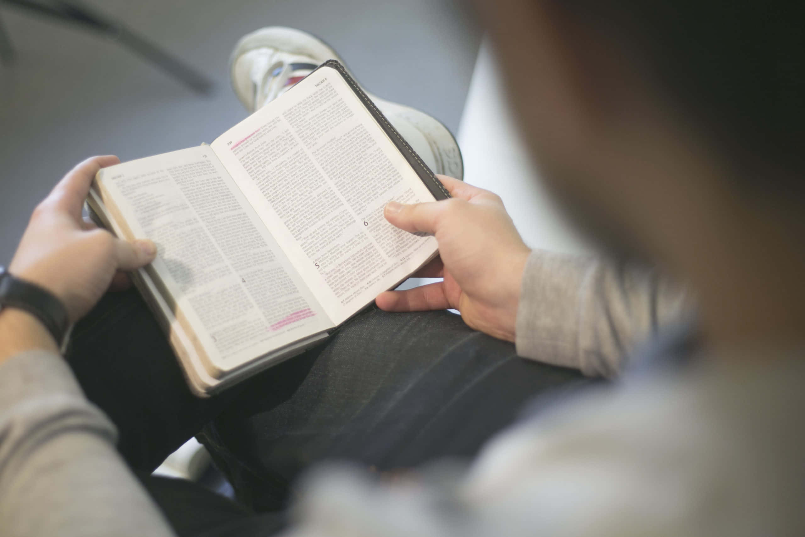 一個人穿著運動鞋坐在室內閱讀一本書。
