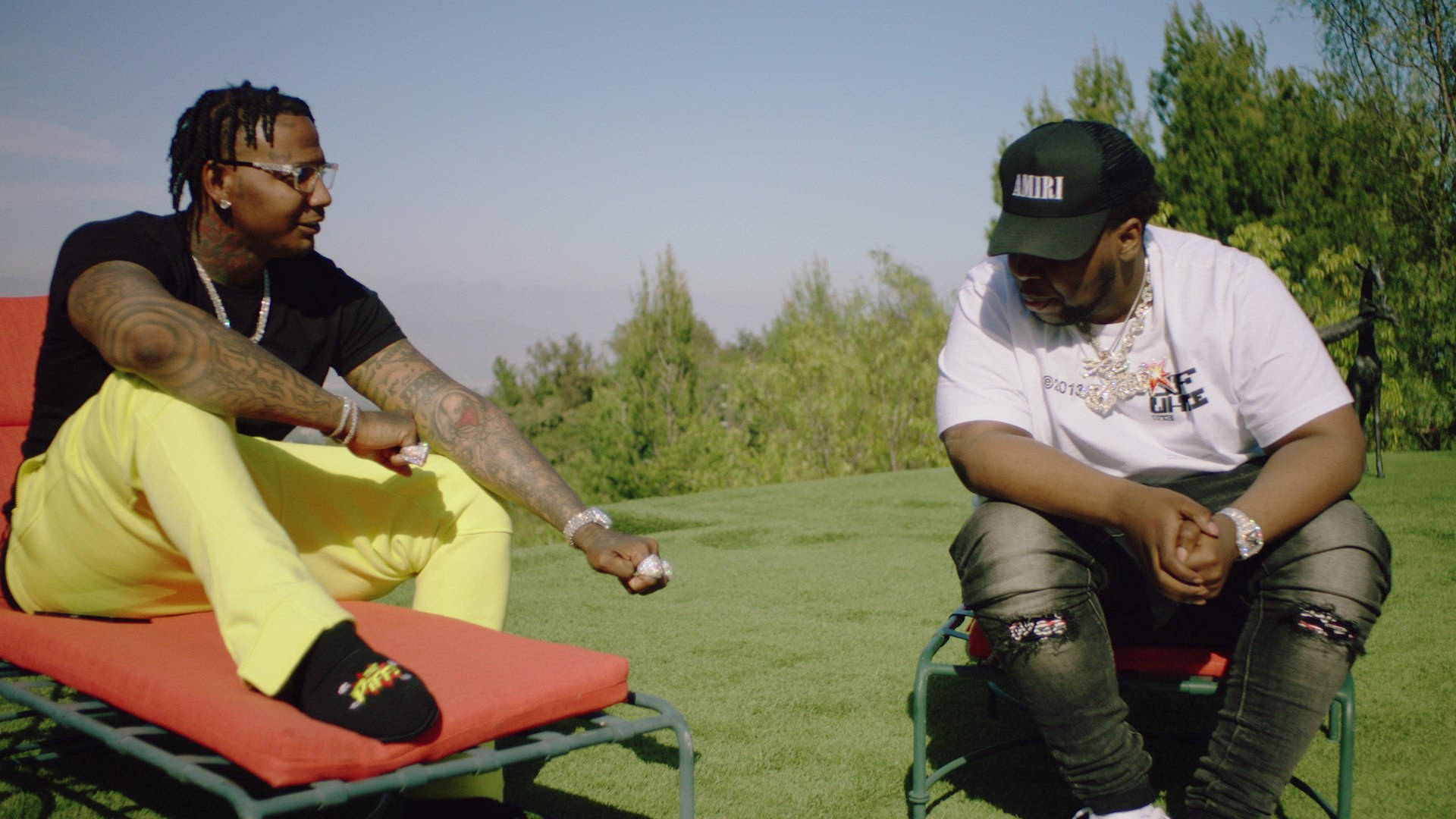 Big 30 與 Moneybagg Yo 壁紙 — 兩名身穿時尚街頭服飾的男子坐在紅色休閒椅上，位於修剪整齊的草坪上，頭頂是清澈的藍天。