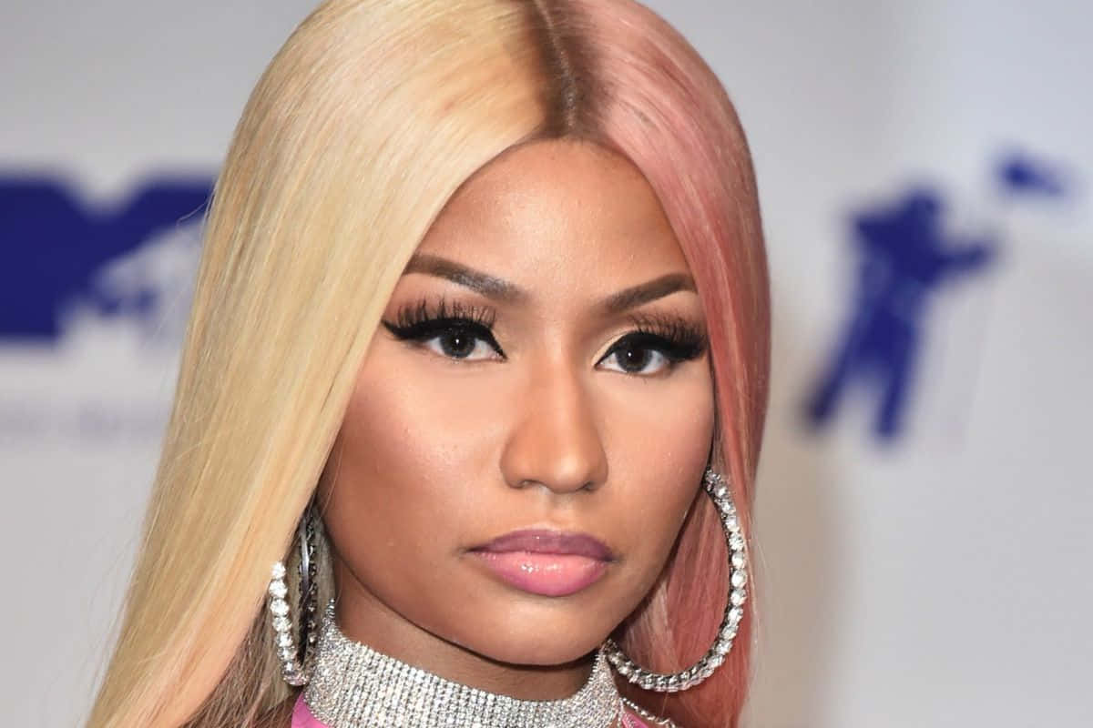 妮琪·米娜在《Big Bank》音樂影片中展現活力 壁紙 — Nicki Minaj 的頭像特寫，金髮和粉紅色頭髮，戴著鑽石耳環和閃閃發光的頸鏈。