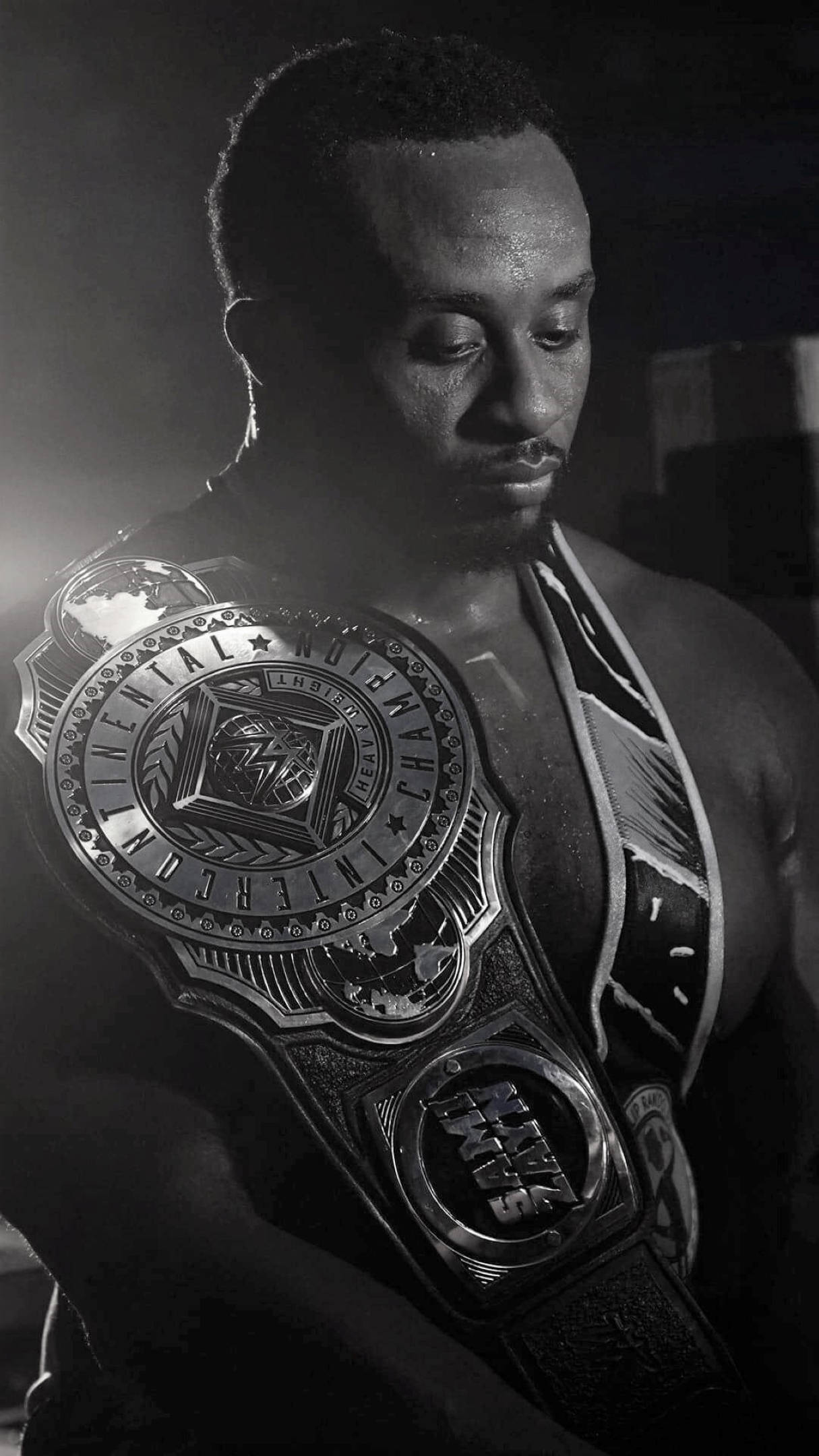Big E 黑白照片 壁紙 — 一位肌肉發達的摔角手在黑白畫面中，於戲劇性燈光下專注地舉起冠軍腰帶。