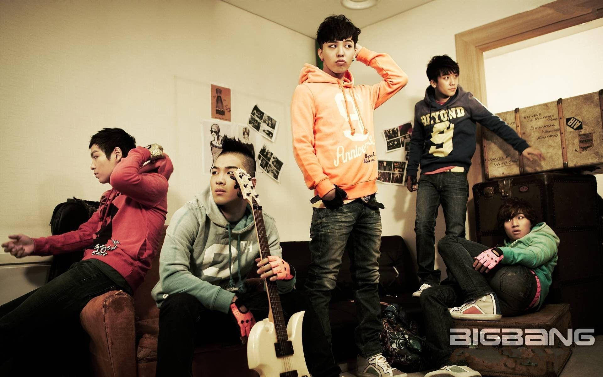 Bigbang 男子團體海報 壁紙 — 五個穿著休閒服的年輕男子在一個雜亂的房間裡戲劇性地擺姿勢，房間裡有復古行李箱和牆上照片。