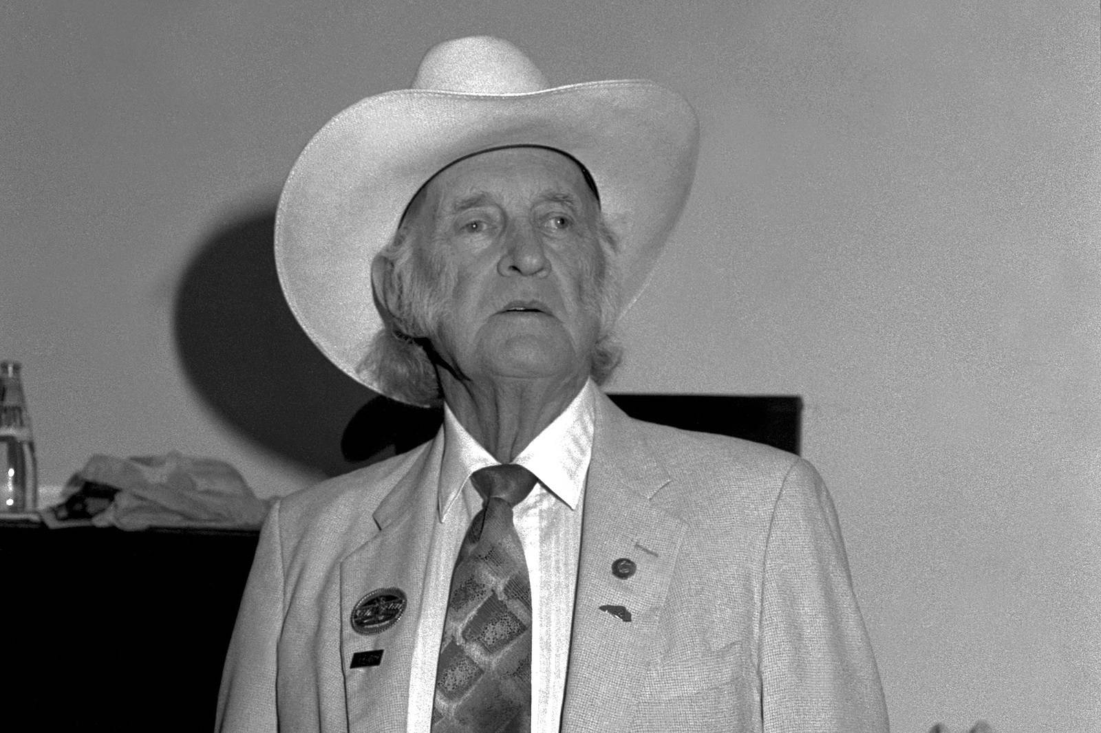 Bill Monroe 在芝加哥老城民謠學校 壁紙 — 一位戴白色牛仔帽、穿西裝的長者，在黑白照片中莊嚴地站在素色背景前。